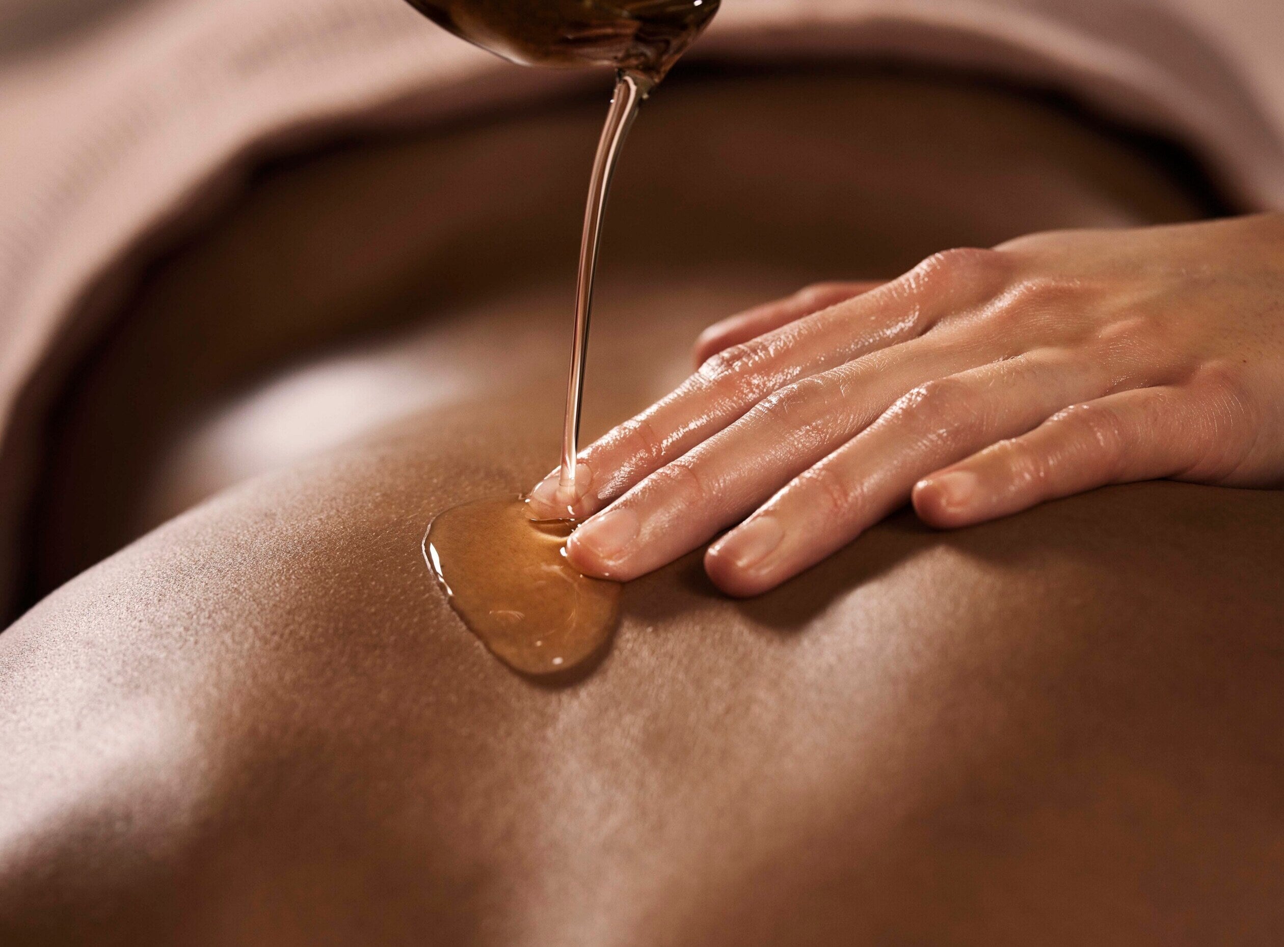 huile en train d'être versée sur un dos. Une main placée sur le dos indique le début d'un massage