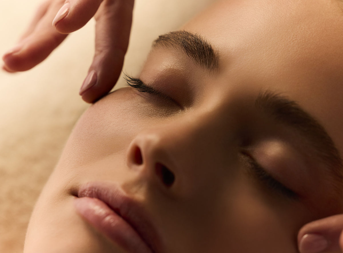 Gros plan sur le visage d'une femme aux yeux fermés, les doigts d'une praticienne posés au coin de son œil