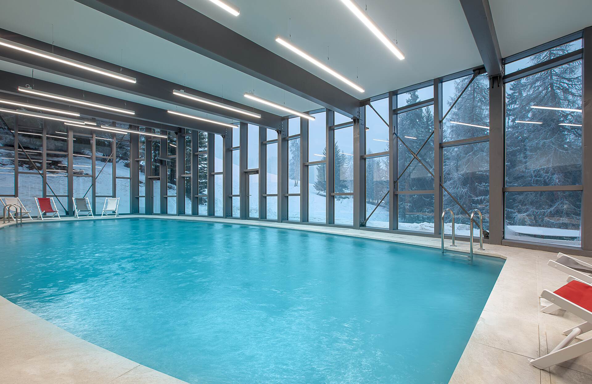Une piscine intérieure spacieuse s’ouvre sur de grandes baies vitrées offrant une vue directe sur un paysage enneigé, tandis que l’eau turquoise occupe largement l’espace.
L’architecture moderne, les lignes épurées et la lumière naturelle créent une atmosphère à la fois immersive et apaisante, idéale pour une expérience bien‑être en pleine nature.