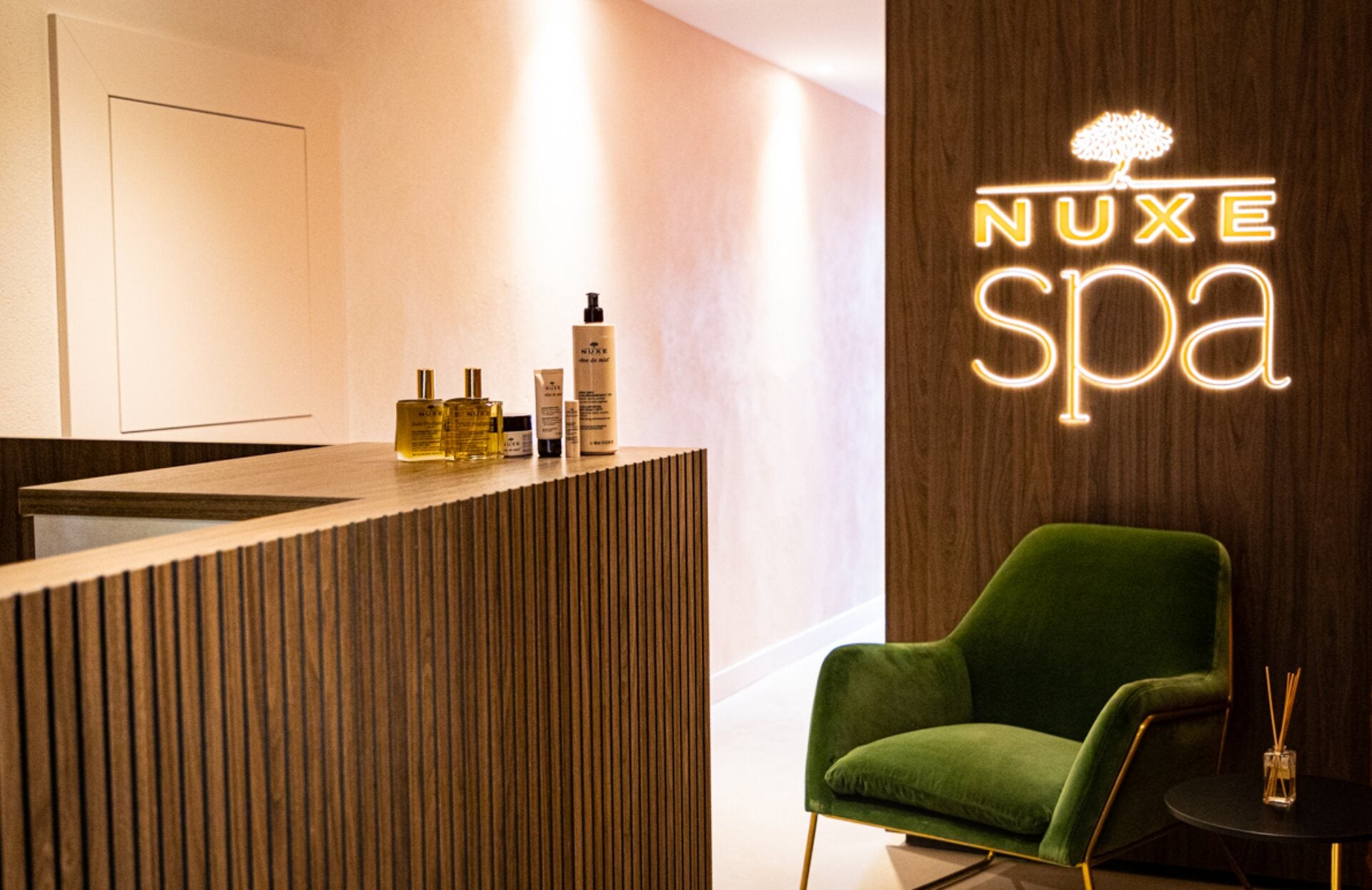 Un espace d’accueil élégant et chaleureux, où le bois et la lumière douce créent une atmosphère apaisante. Sublimé par l’enseigne lumineuse “Nuxe Spa”, ce lieu raffiné, agrémenté de produits iconiques et d’un fauteuil confortable, invite d’emblée à une expérience de bien‑être unique et sensorielle.