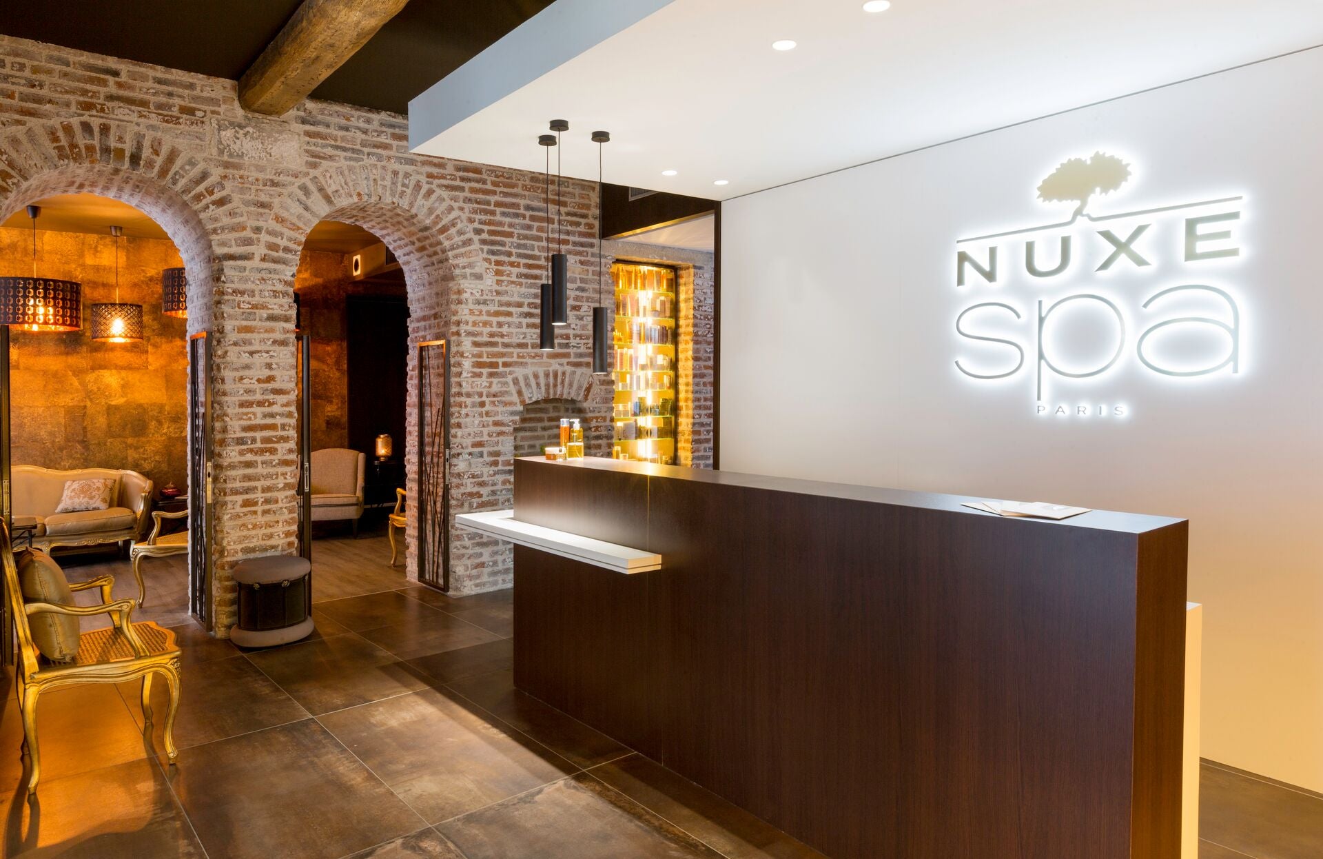 Voici une proposition de texte pour cette image :
Un espace d’accueil élégant et raffiné aux accents chaleureux, mêlant pierres apparentes et matériaux contemporains. Dominé par une réception épurée et sublimé par l’enseigne lumineuse “Nuxe Spa Paris”, ce lieu invite dès l’entrée à une expérience sensorielle unique, entre authenticité et modernité.