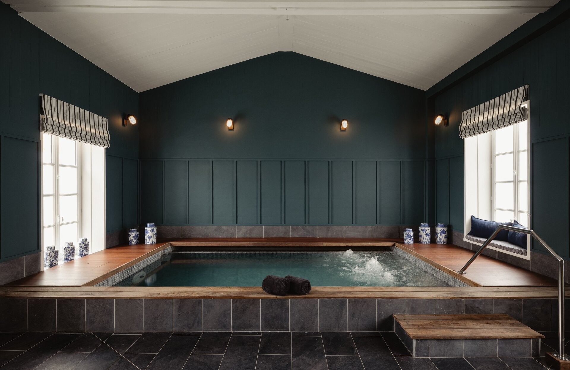 Un espace bien-être élégant et intimiste, habillé de tons profonds et apaisants, accueille un bassin chauffé aux bulles relaxantes. Entouré de bois et de céramique, cet espace offre une atmosphère chaleureuse, sublimée par une lumière douce et de larges fenêtres qui apportent une belle luminosité naturelle.