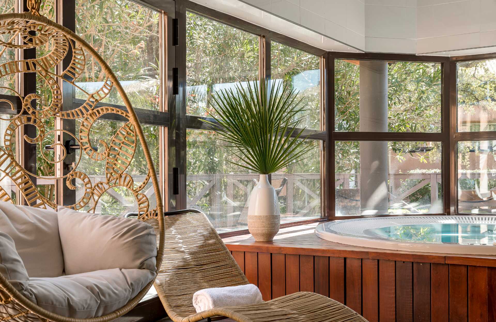 Un espace de détente baigné de lumière naturelle, où les matières naturelles et les larges baies vitrées créent une atmosphère apaisante. Entre fauteuil suspendu, transat confortable et jacuzzi intimiste, ce lieu invite à un moment de relaxation totale au cœur d’un environnement verdoyant.