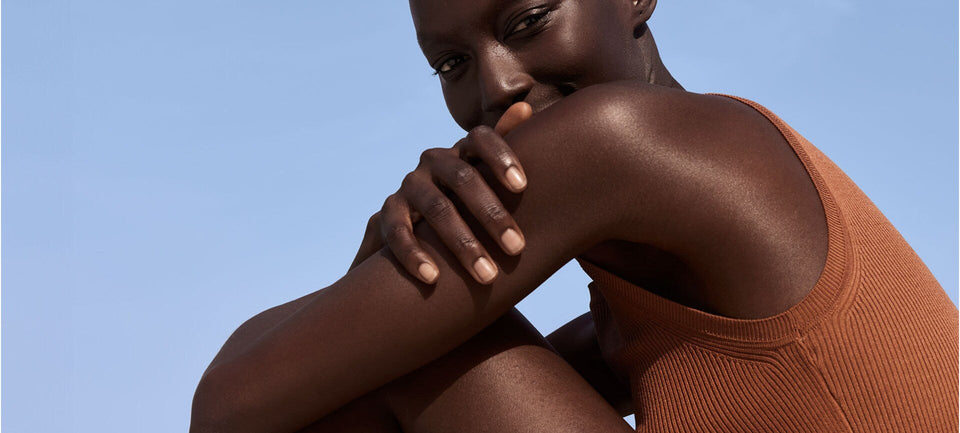 femme sur fond ciel. Elle est assise et croise ses bras autour de ses genoux. Elle regarde l'objectif - regard doux et bienveillant. Elle semble apaisée