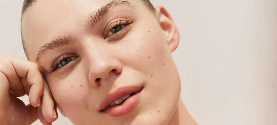 visage d'une femme sur fond beige. Elle appuie sa tête contre sa main. Elle regarde l'objectif, elle est sereine, détendue