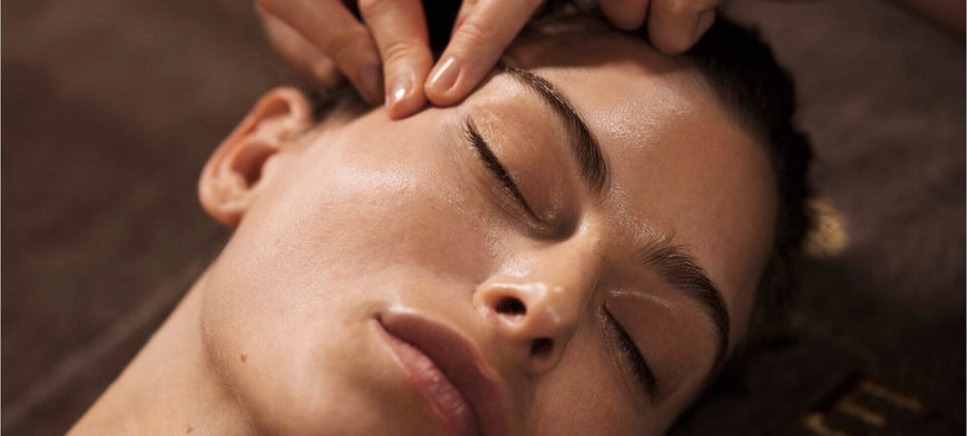 visage d'une femme détendue, les yeux fermés se faisant masser le contour de l'œil par deux doigts