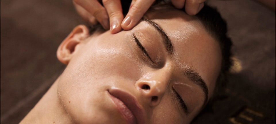 visage d'une femme détendue, les yeux fermés se faisant masser le contour de l'œil par deux doigts