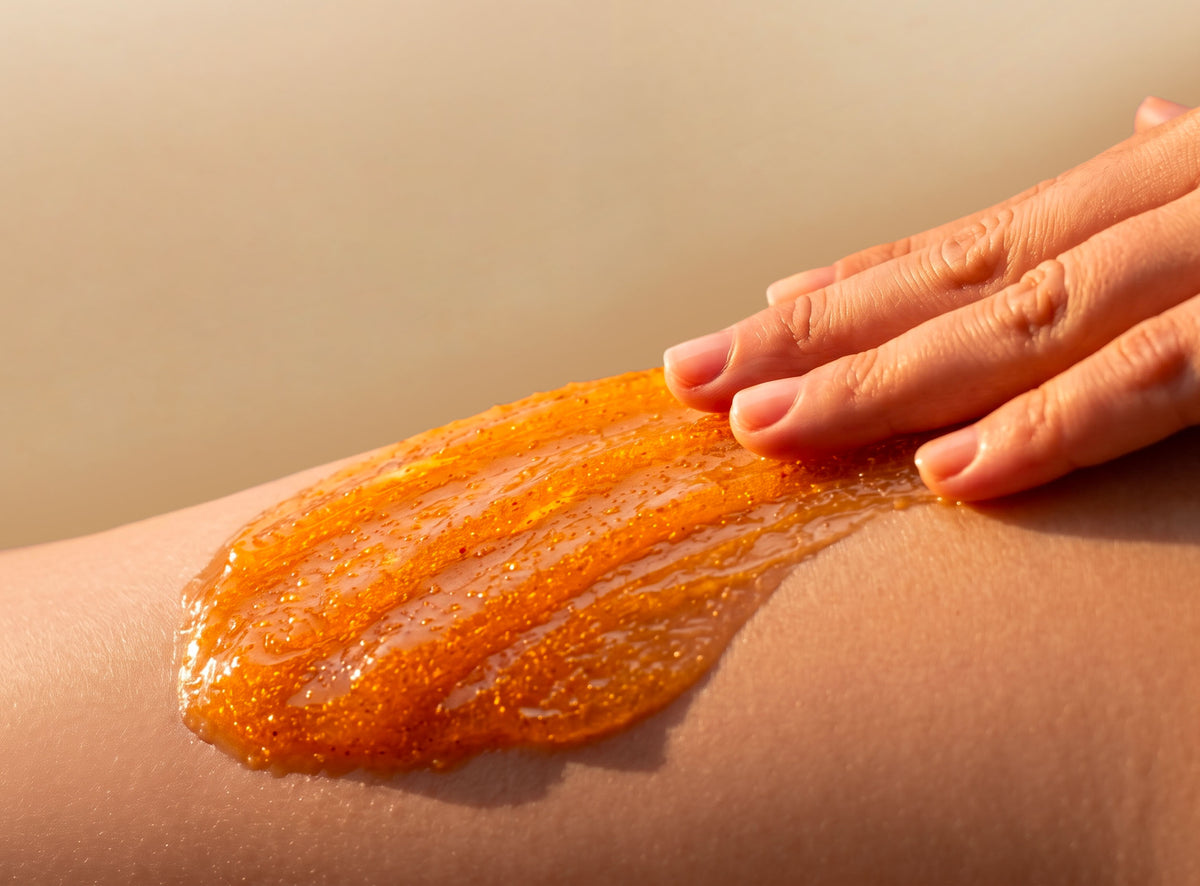 Main appliquant un gommage exfoliant orangé sur la peau.