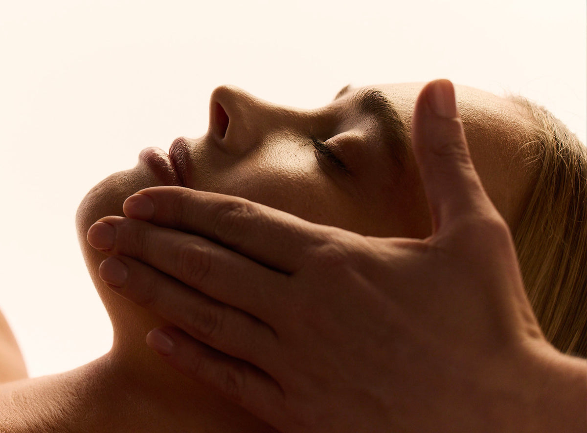 Femme allongée les yeux fermés, le visage détendu, pendant qu'une main masse doucement sa mâchoire
