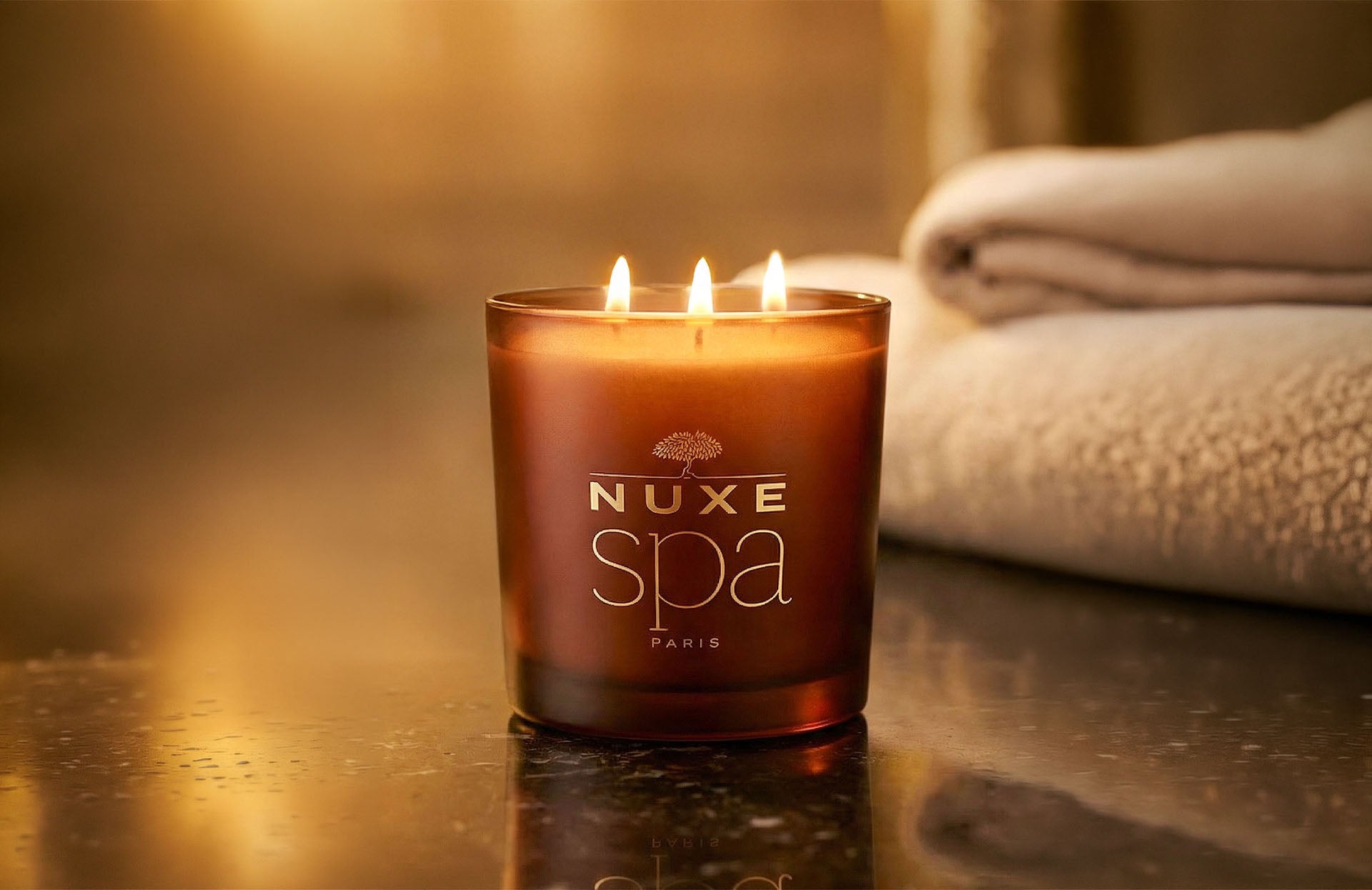 bougie de la marque NUXE SPA posée sur une surface en marbre noir. Les trois mèches sont allumées.