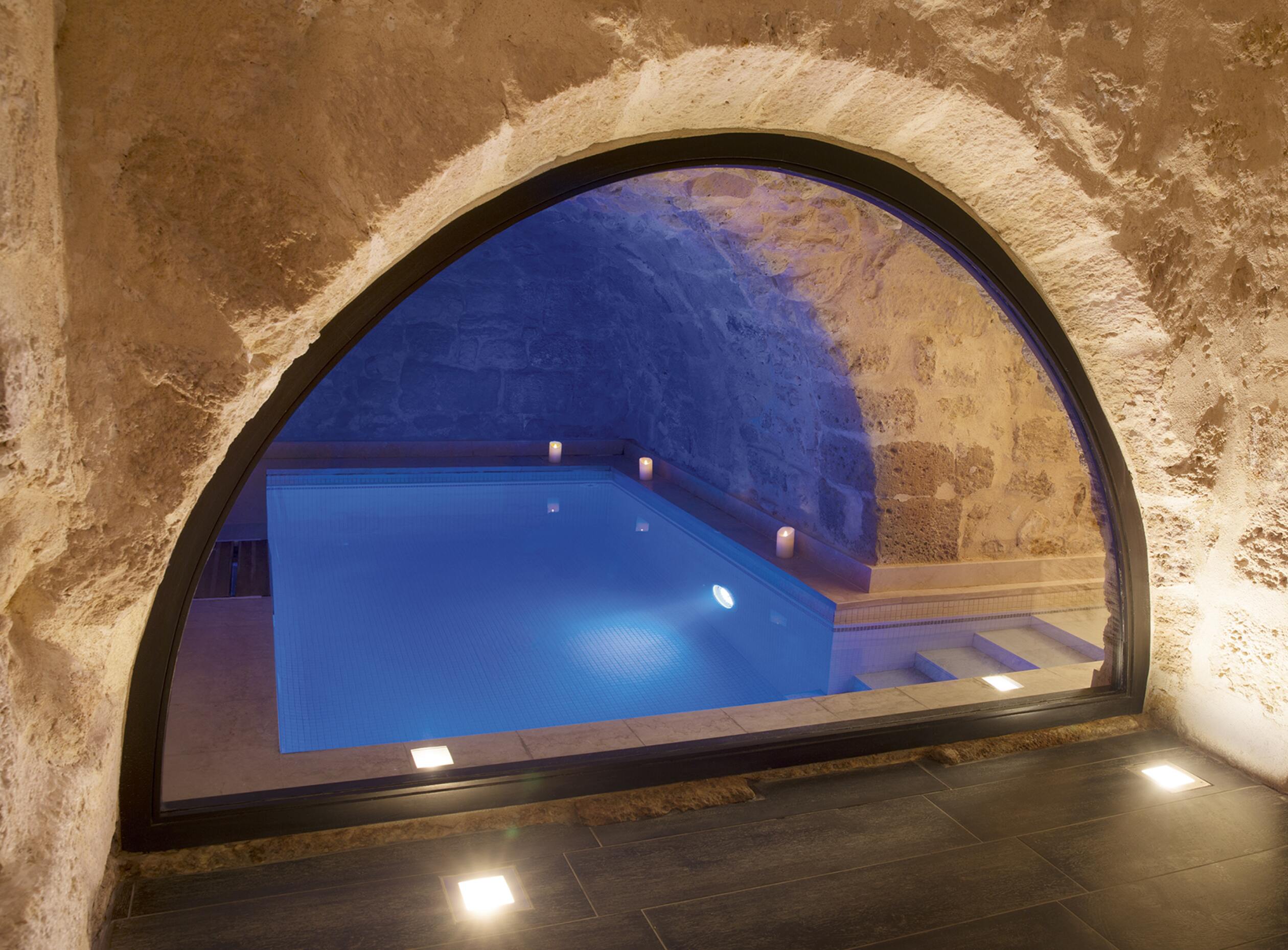 petite piscine intérieure sous une arche en pierre. La lumière est tamisée. 