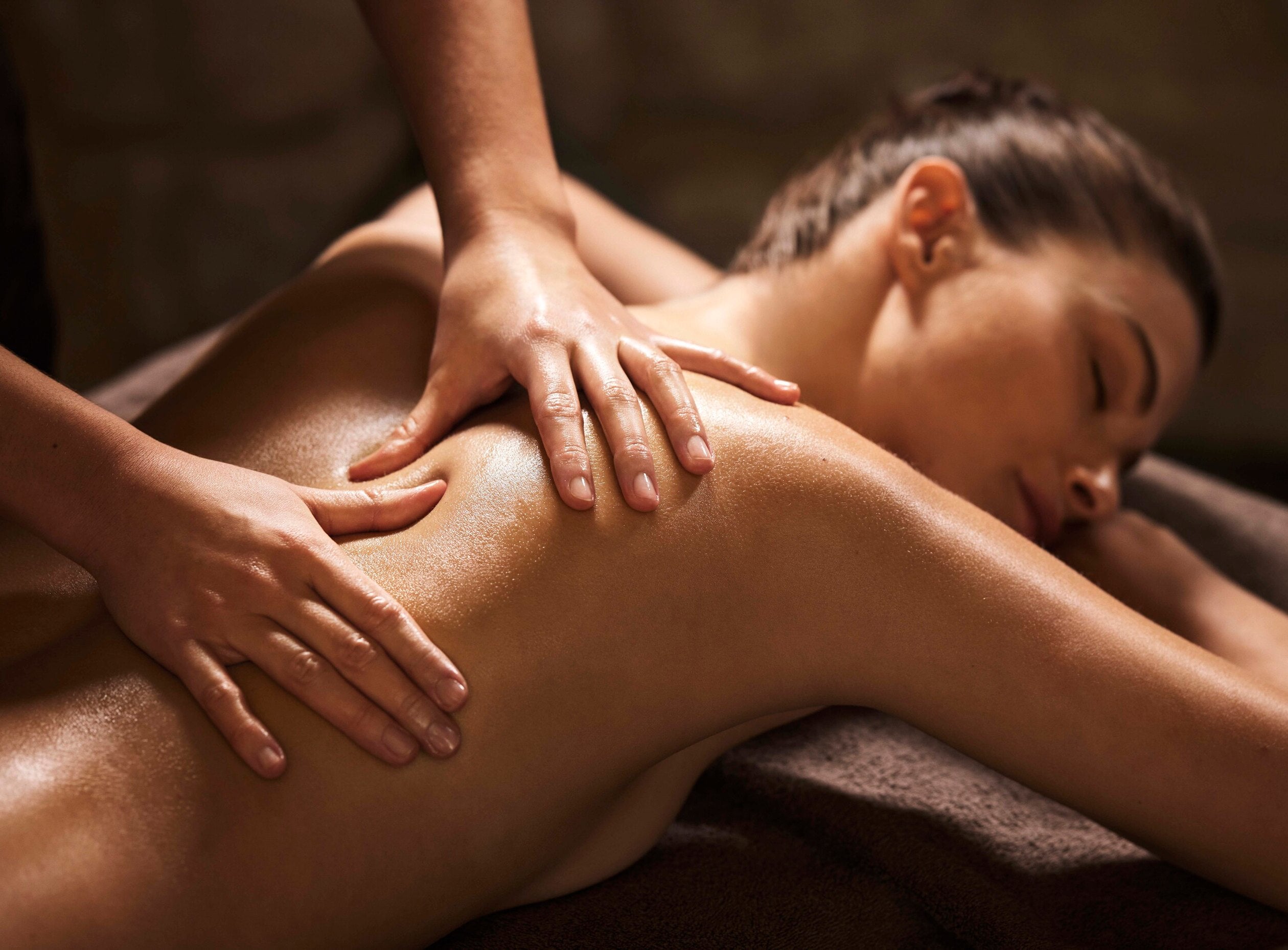 femme allongée sur le ventre sur une table de massage. Elle a les yeux fermés et semble détendue. Deux mains lui massent le dos en appuyant autour de ses omoplates.