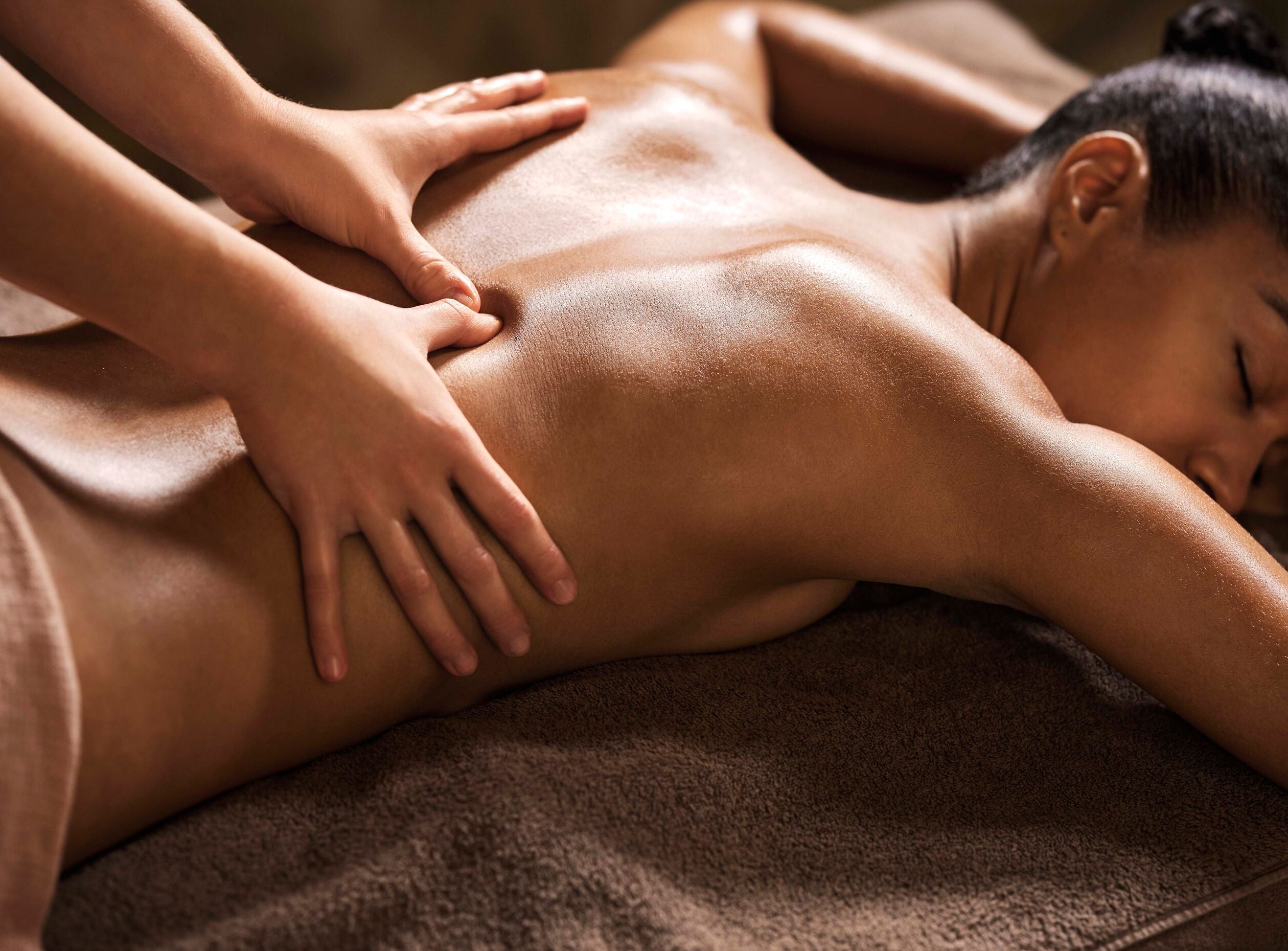 dos et visage d'une femme allongée sur une table de massage. ses yeux sont fermés et elle semble détendue. Deux mains lui massent le dos en faisant glisser leur pouce autour de sa colonne vertébrale