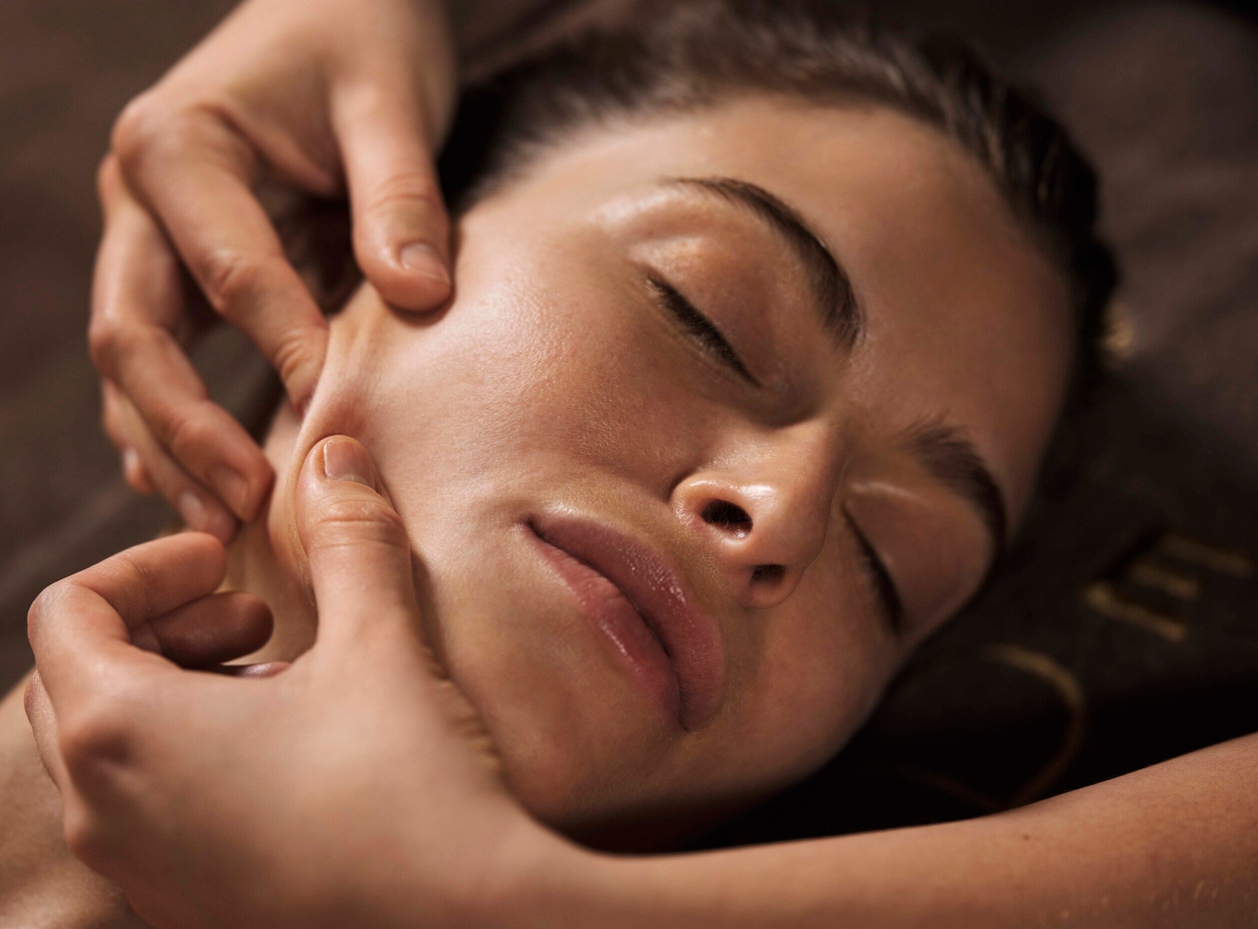 visage d'une femme en train de se faire masser la joue. Elle ferme les yeux et a l'air détendue.