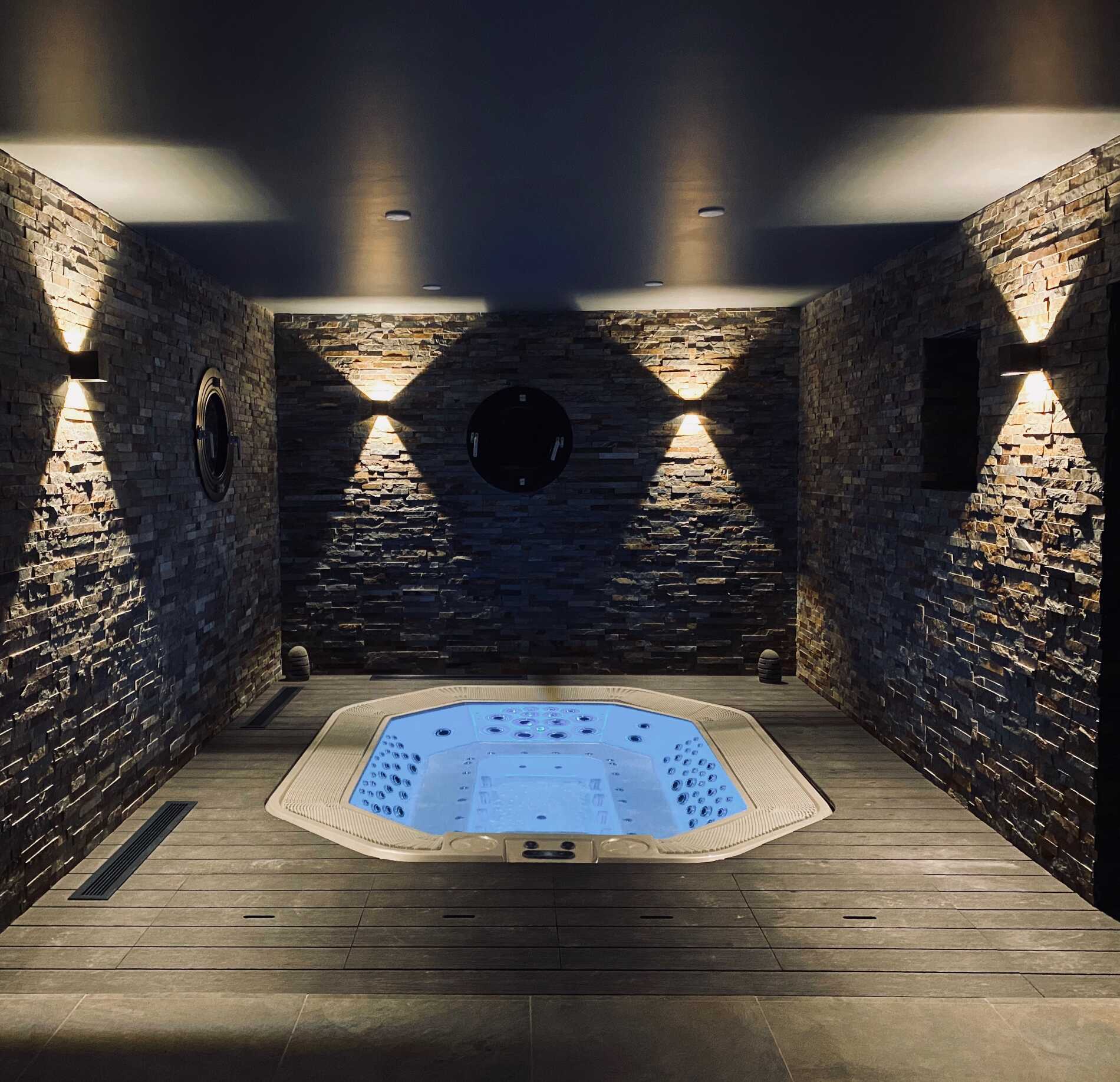 Espace bien-être de l'hôtel 16 150, intimiste avec jacuzzi encastré, entouré de murs en pierre naturelle et sublimé par un éclairage tamisé qui met en valeur les textures minérales, créant une atmosphère élégante, chaleureuse et profondément relaxante.