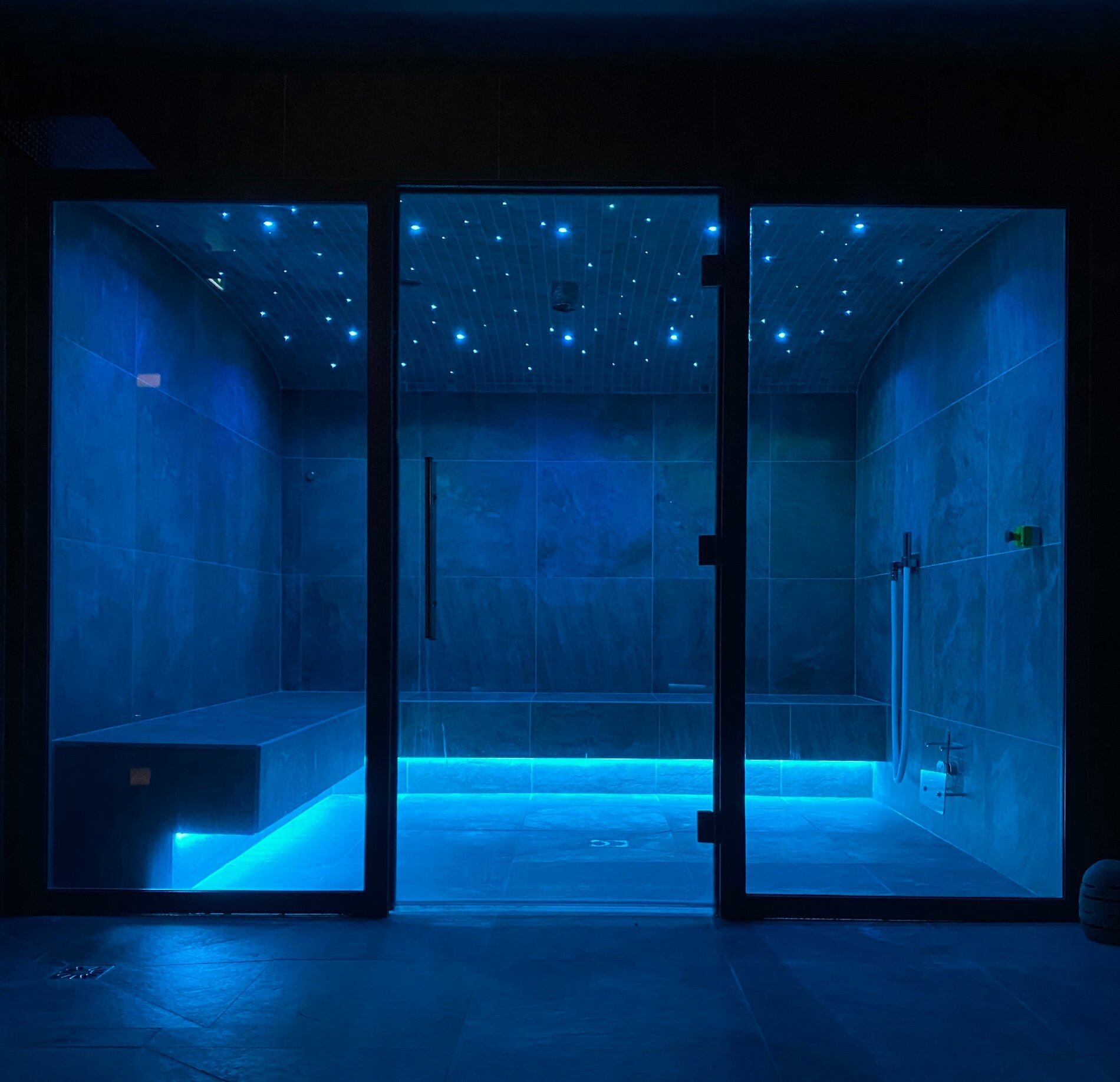 Hammam contemporain du spa NUXE à Vars, enveloppé d’une lumière bleutée apaisante, avec parois minérales élégantes, bancs de relaxation et plafond étoilé créant une atmosphère immersive, sereine et profondément relaxante.