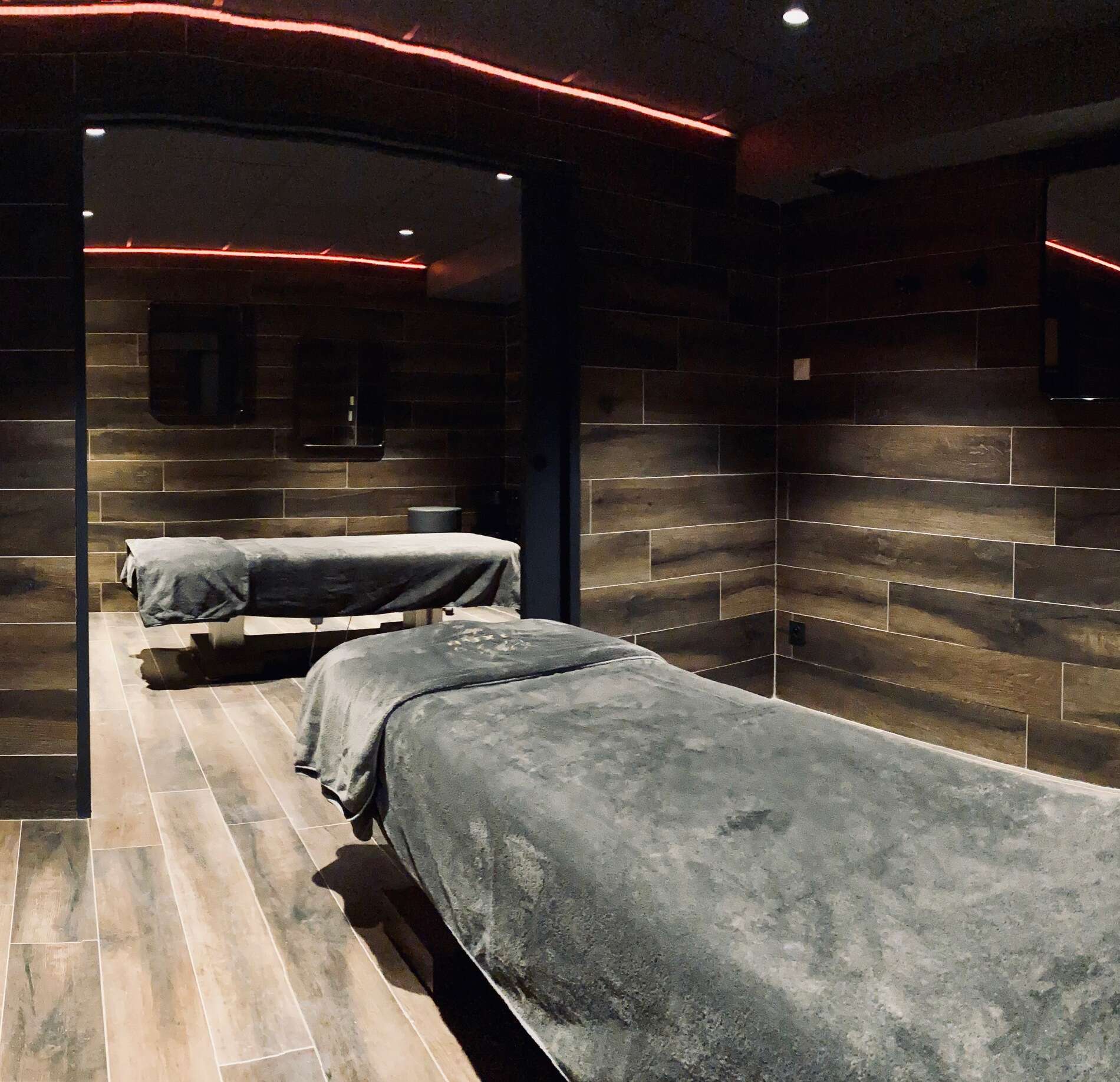 Cabine de soin intimiste du spa NUXE, habillée de bois sombre élégant, avec tables de massage confortables, éclairage tamisé aux accents rouges et ambiance feutrée créant une atmosphère profonde et relaxante.