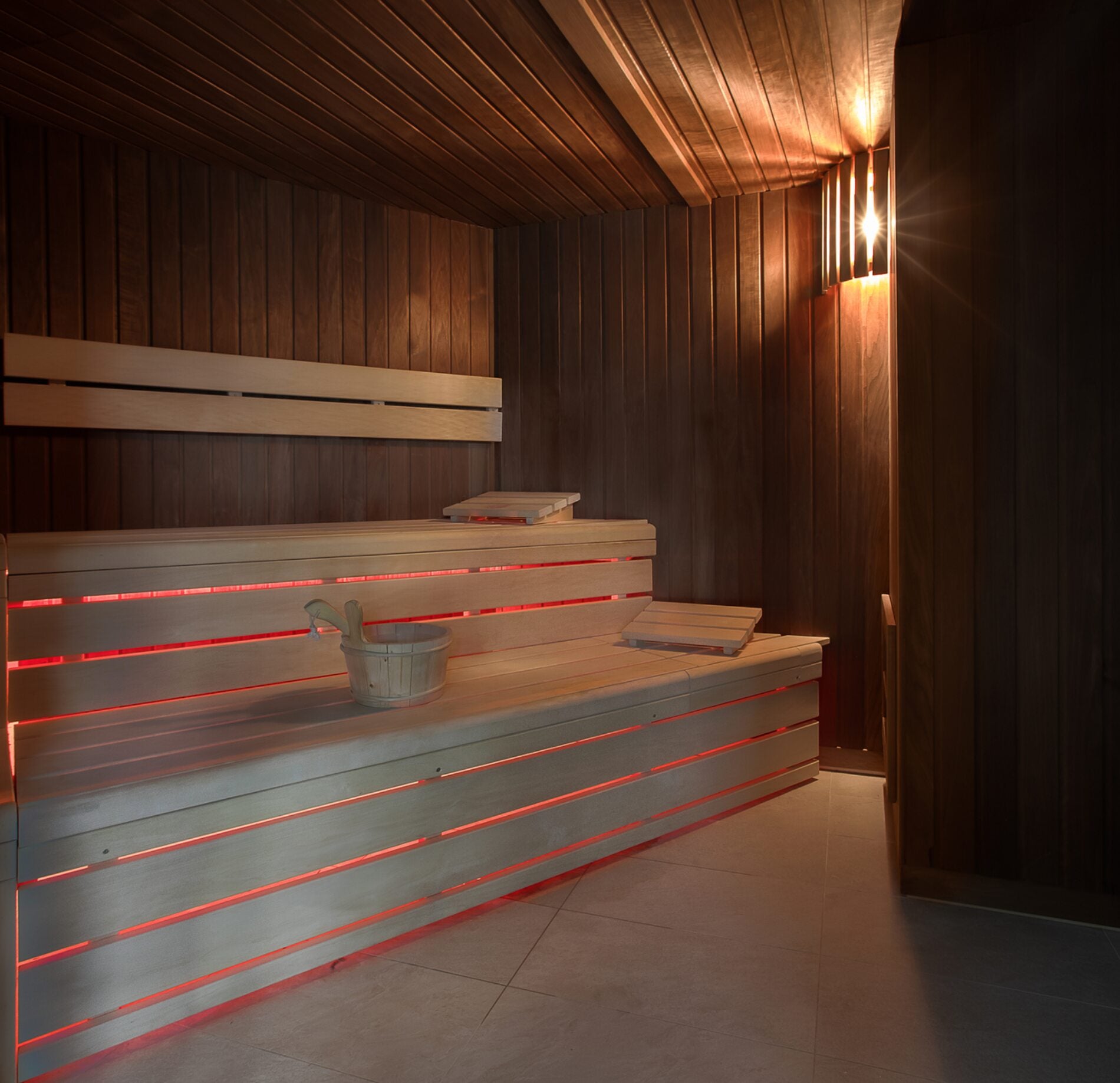  Sauna élégant du spa Altezza Les Arcs, habillé de bois chaleureux et baigné d’une lumière douce, avec des banquettes confortables soulignées par un éclairage subtil.