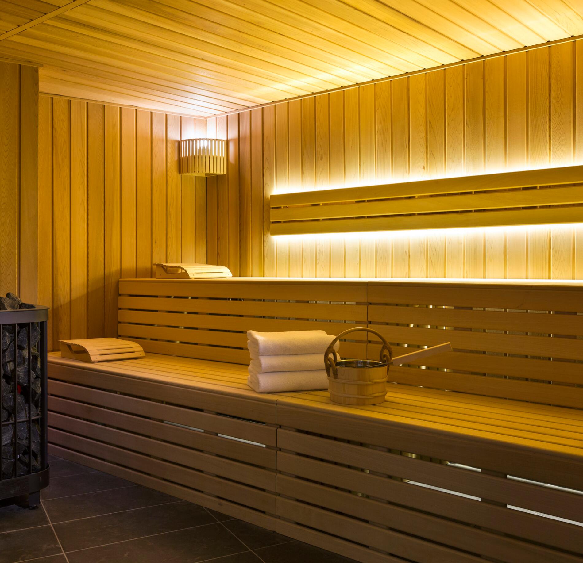 Sauna élégant du spa NUXE à l'araucaria, entièrement habillé de bois clair, avec banquettes spacieuses, éclairage chaleureux et accessoires traditionnels, créant une atmosphère lumineuse, apaisante et haut de gamme. 