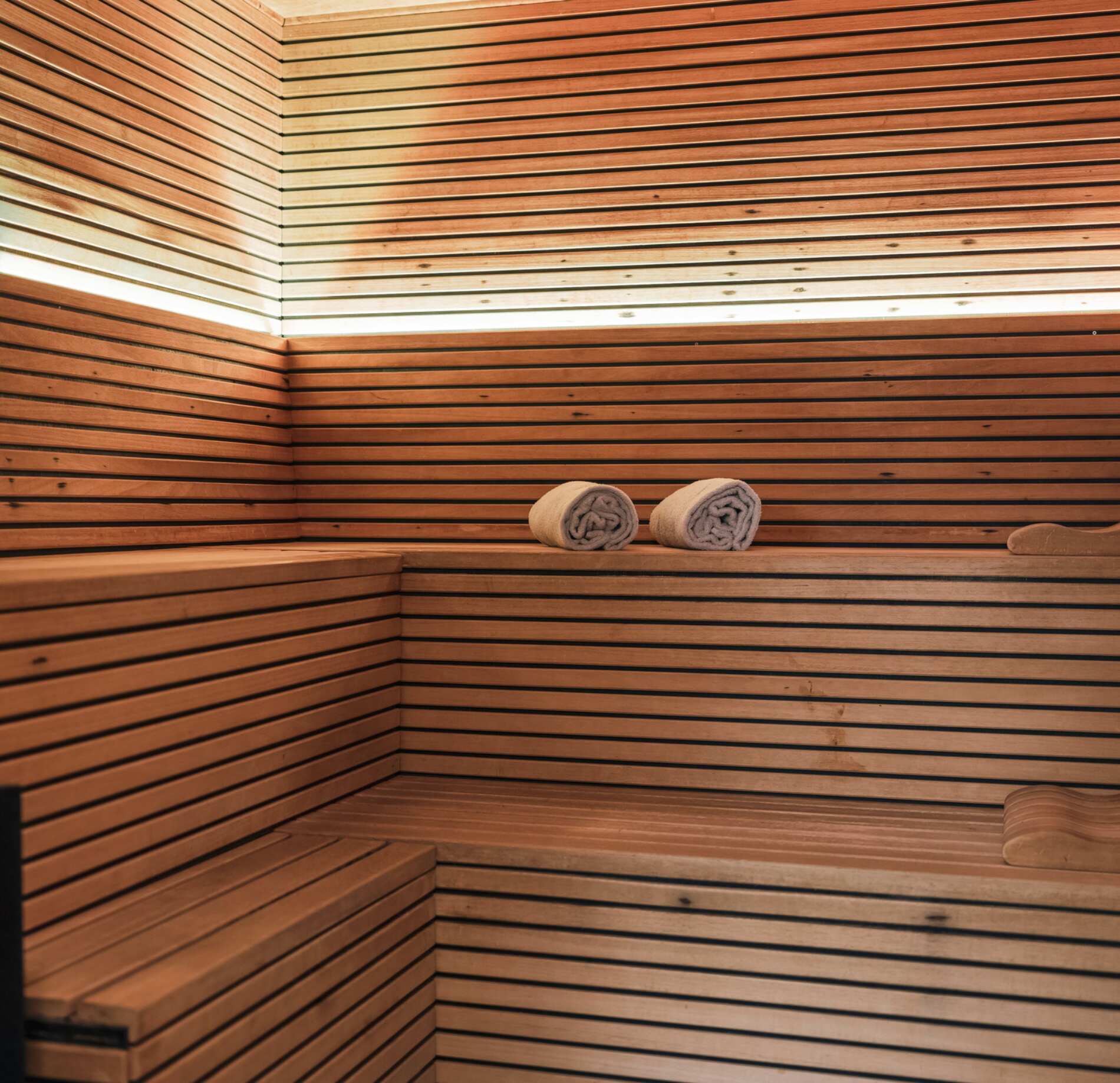 Sauna élégant du spa NUXE à l’Hôtel Balthazar, entièrement habillé de bois aux lignes épurées, avec banquettes spacieuses et serviettes roulées, baigné d’une lumière chaleureuse créant une atmosphère intime et profondément relaxante.