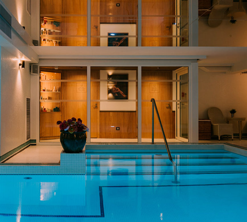 Bassin intérieur de bien-être au spa NUXE de l'hôtel le grand tonic, sublimé par une eau claire et des éclairages doux, avec un accès par marches et de larges baies vitrées donnant sur des espaces boisés élégants, créant une ambiance intime et haut de gamme. 