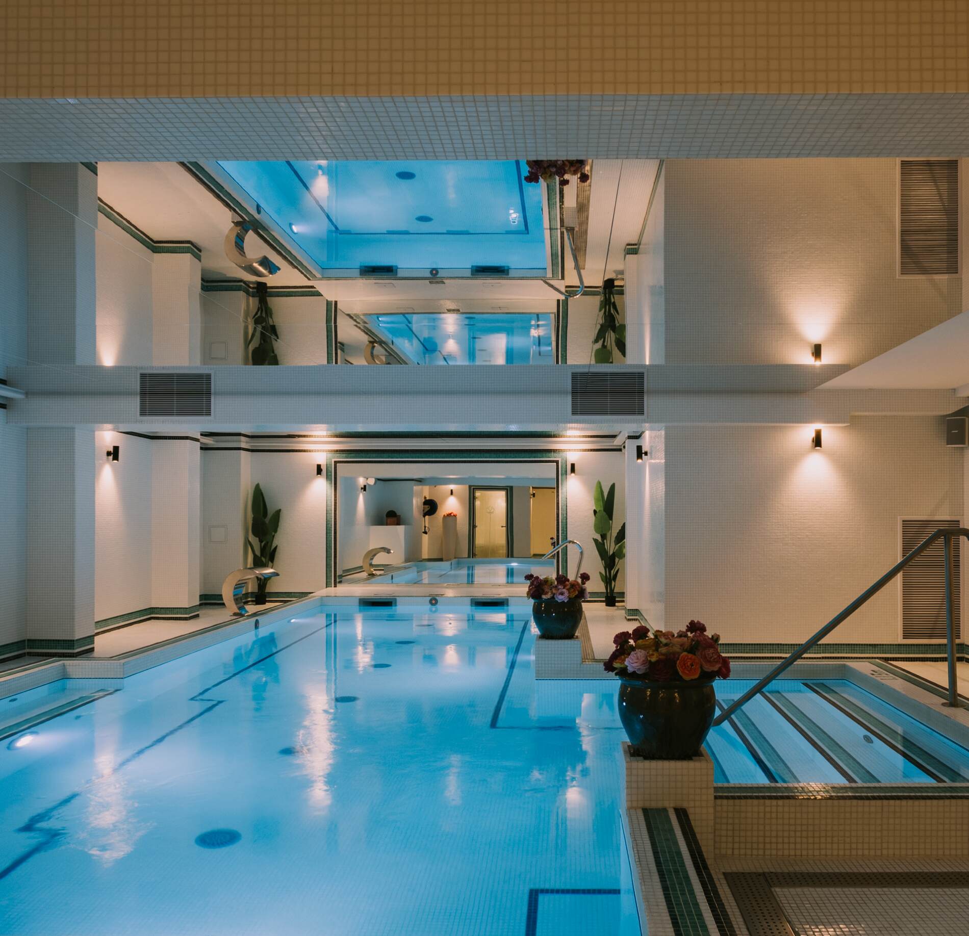 Piscine intérieure lumineuse du spa NUXE de l'hôtel le grand tonic, avec eau turquoise apaisante, escaliers immergés et architecture élégante sur plusieurs niveaux, sublimée par des éclairages doux et des compositions florales raffinées créant une atmosphère sereine et haut de gamme. 