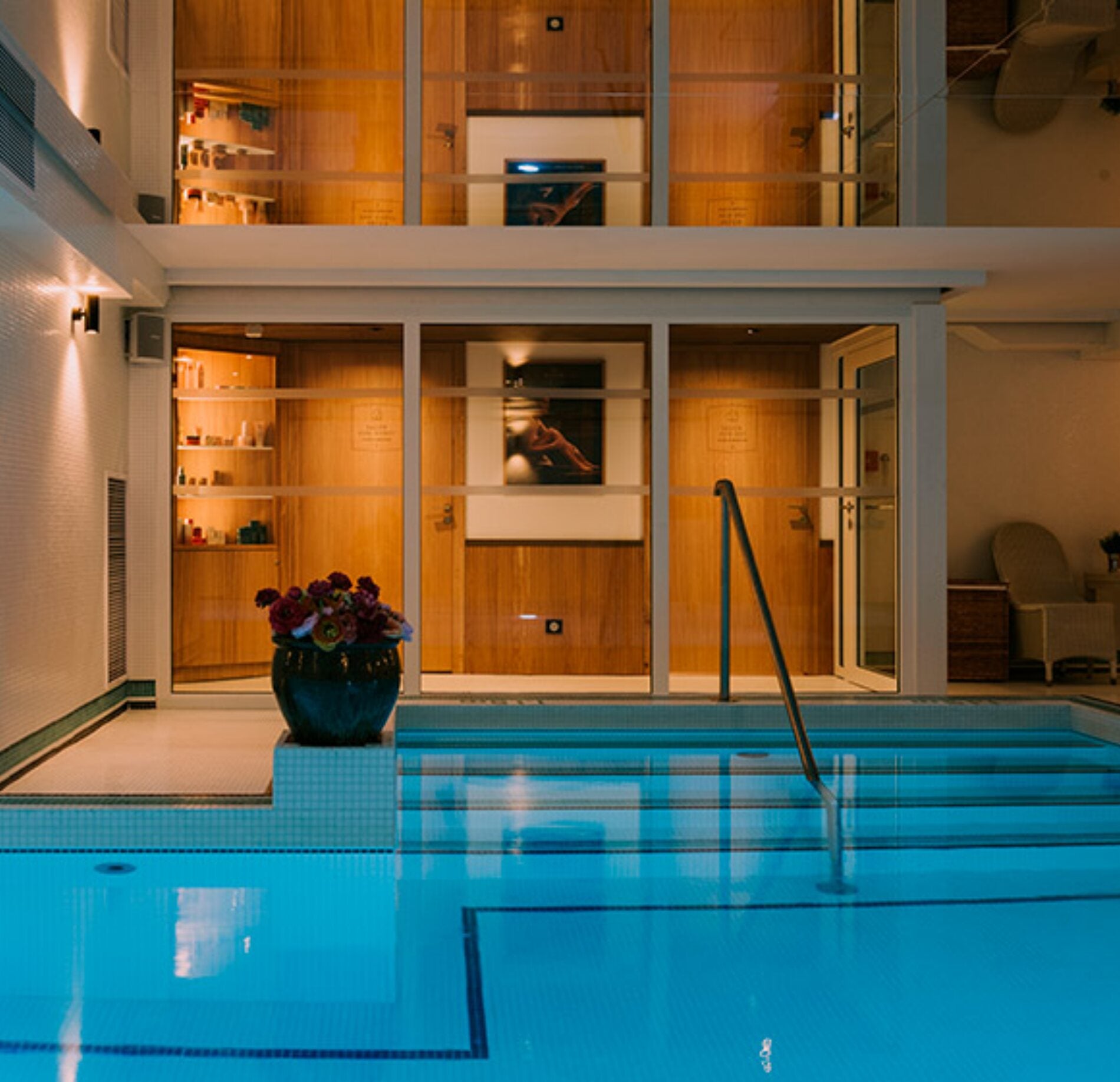 Piscine intérieure élégante du spa NUXE, avec eau turquoise lumineuse, escalier immergé et grand espace vitré dévoilant des cabines en bois chaleureuses, dans une atmosphère raffinée et apaisante.