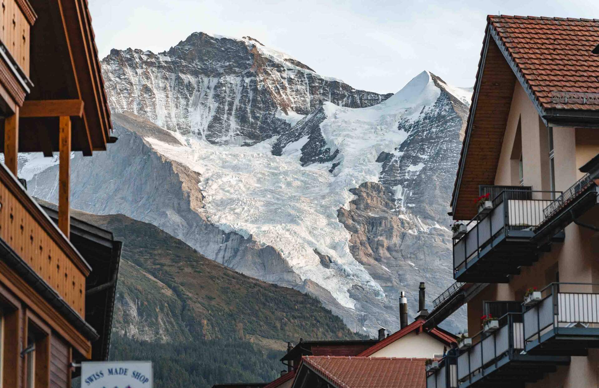 Une vue spectaculaire encadrée par des chalets en bois révèle une montagne majestueuse aux sommets enneigés et aux reliefs marqués, dominant le paysage.
Les contrastes entre les toits chaleureux, la roche brute et la glace éclatante créent une atmosphère unique, invitant à une expérience alpine immersive et dépaysante.