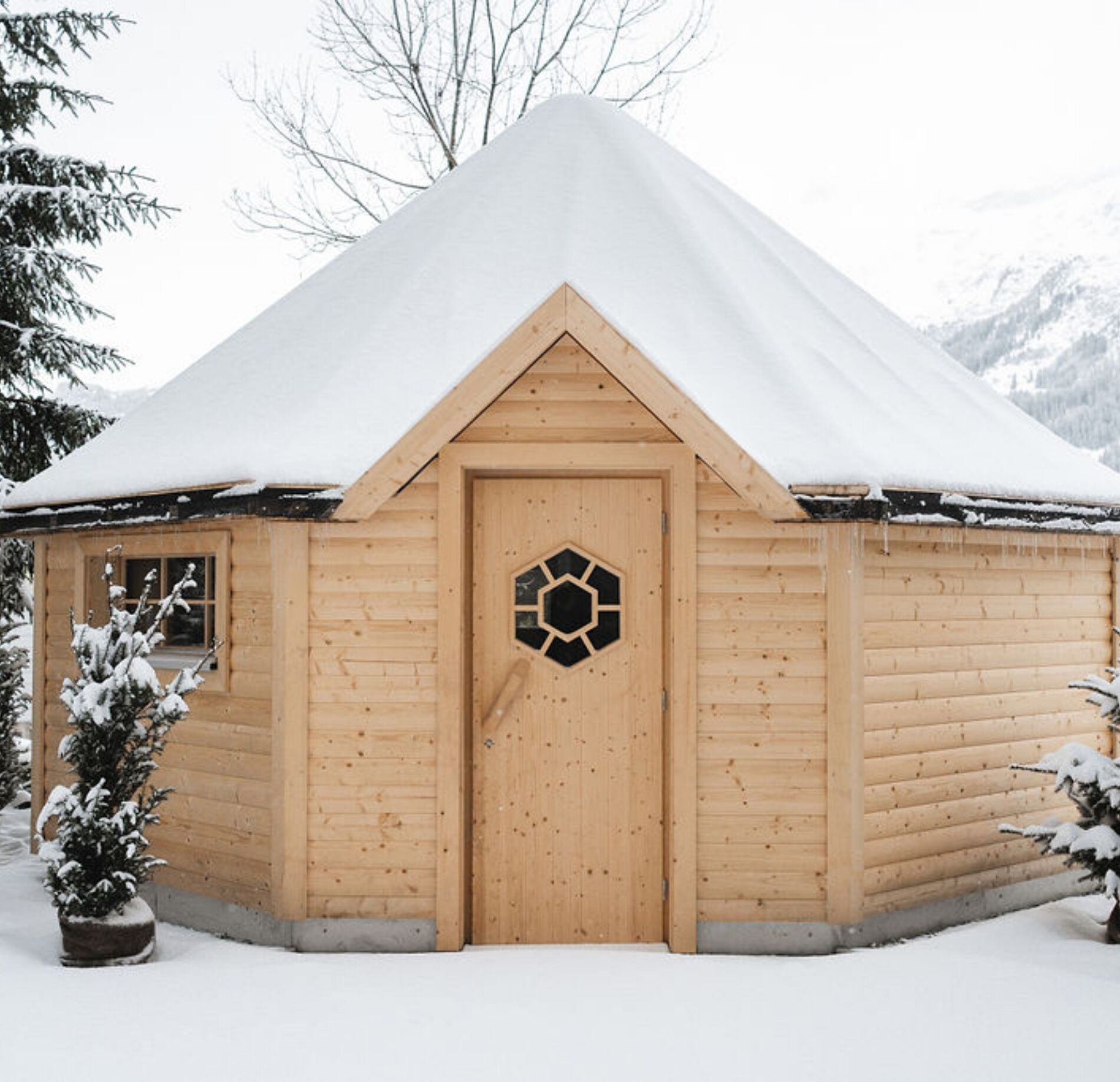 Chalet sauna extérieur du spa NUXE à l’Hôtel Braunbär, en bois clair avec toit enneigé, niché dans un paysage hivernal immaculé entouré de sapins, créant une atmosphère chaleureuse, authentique et ressourçante.