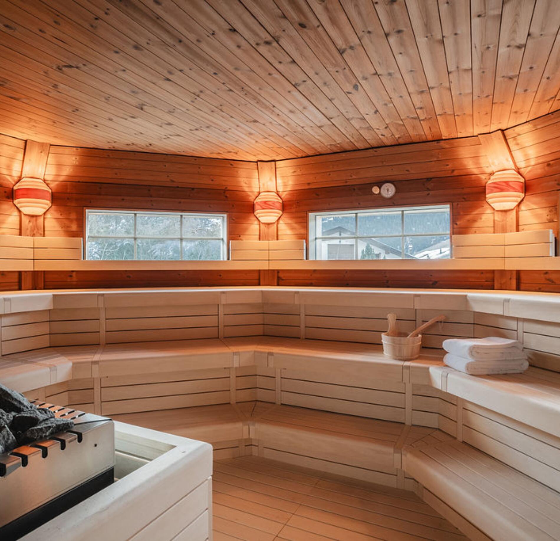 Sauna spacieux et chaleureux du spa NUXE à l’Hôtel Braunbär, avec banquettes en bois clair disposées en gradins, éclairage doux et fenêtres laissant apparaître un paysage hivernal, créant une atmosphère lumineuse, conviviale et profondément relaxante.