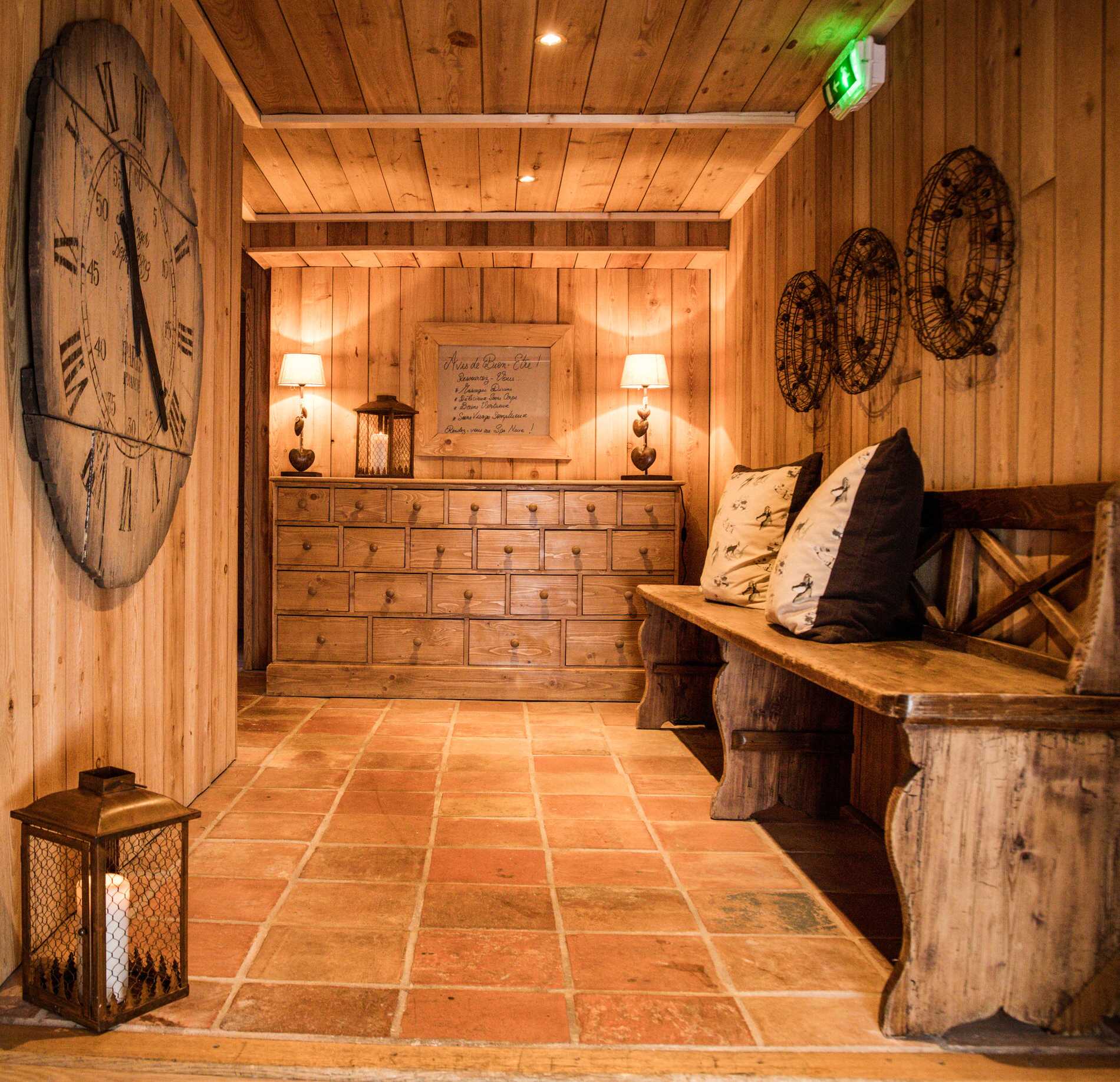 Espace lounge chaleureux du spa NUXE à l’Hôtel Le Chamois, entièrement habillé de bois avec bancs rustiques, coussins confortables, meubles authentiques et éclairage doux, créant une atmosphère cocooning, élégante et apaisante.