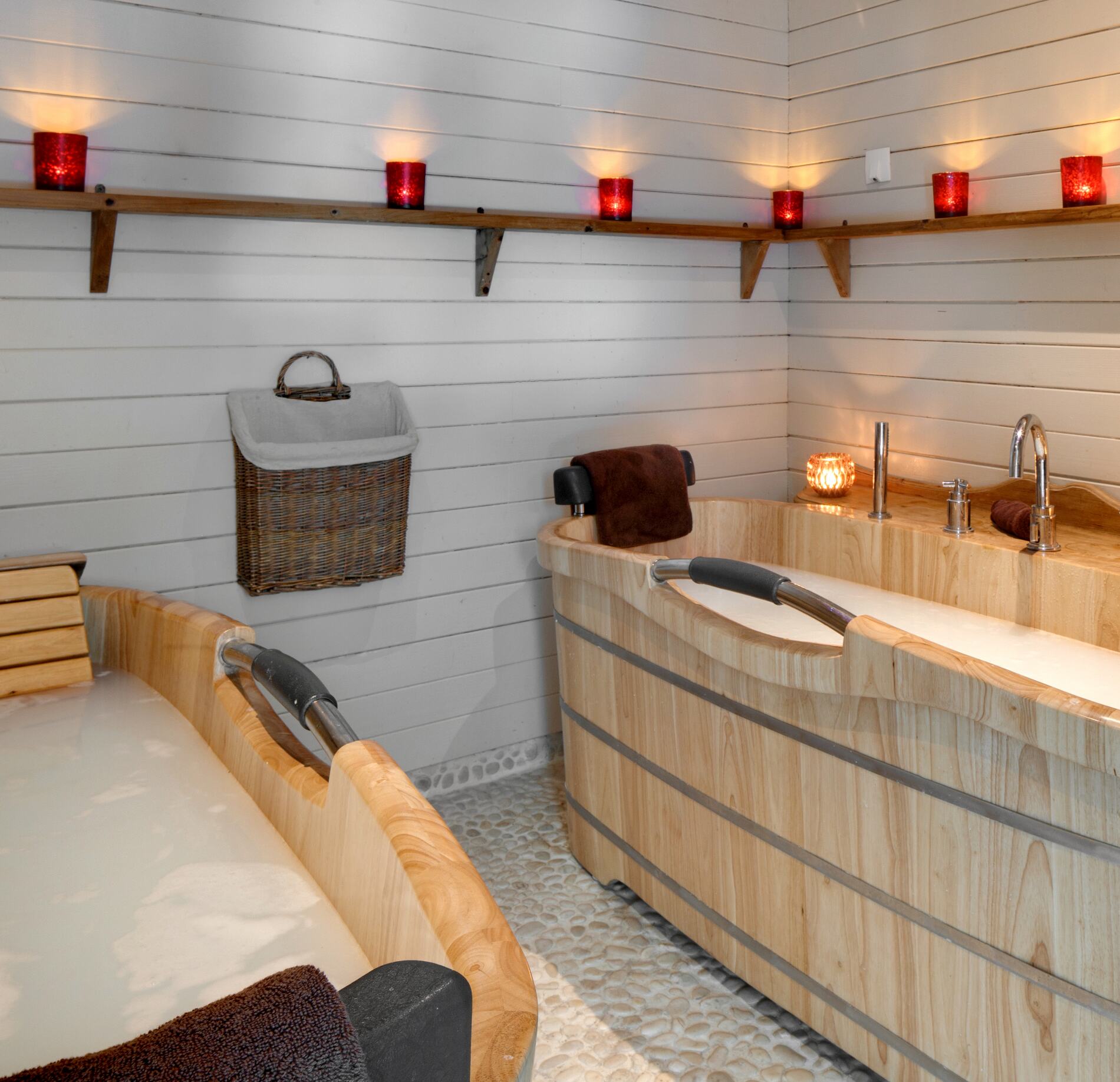 Espace de bain bien-être du spa NUXE à l’Hôtel Le Chamois, avec baignoires en bois clair au design raffiné, éclairage doux par bougies et étagères murales, créant une atmosphère chaleureuse, apaisante et cocooning.