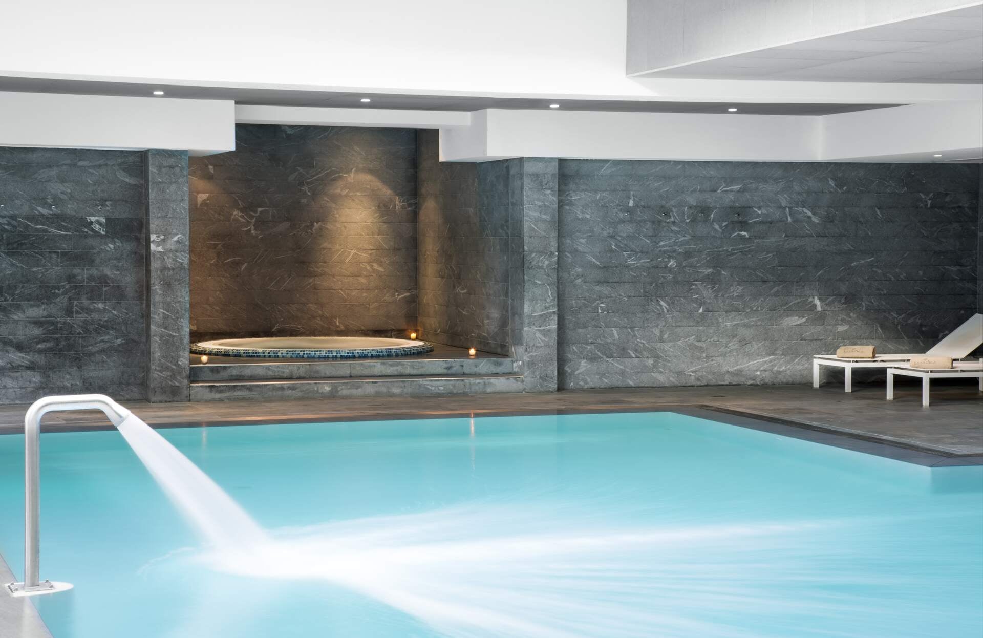 Un espace bien-être élégant et épuré, où une piscine aux lignes contemporaines s’intègre harmonieusement dans un décor minéral aux teintes grisées. À l’arrière, un bain à remous intimiste, sublimé par une lumière douce, invite à une parenthèse de relaxation dans une atmosphère calme et raffinée.