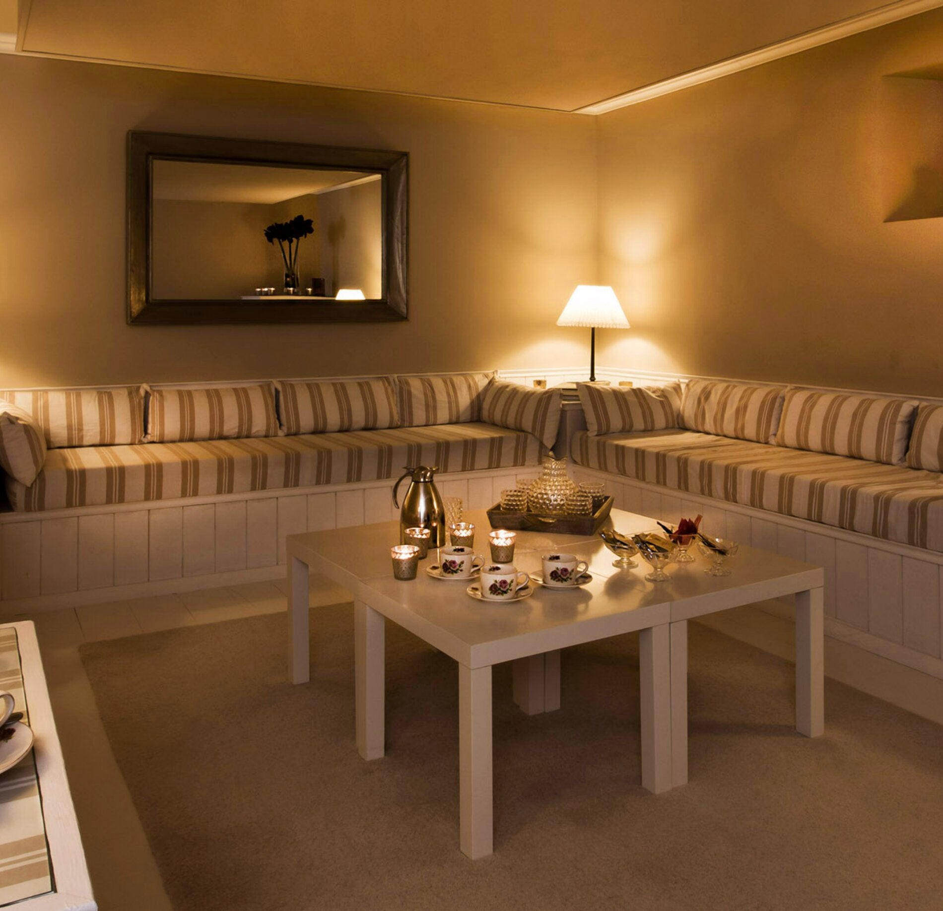 Salon de détente chaleureux et élégant, baigné d’une lumière douce, avec banquettes confortables aux tons neutres, table basse soigneusement dressée pour une pause bien-être et ambiance intime propice à la relaxation. 