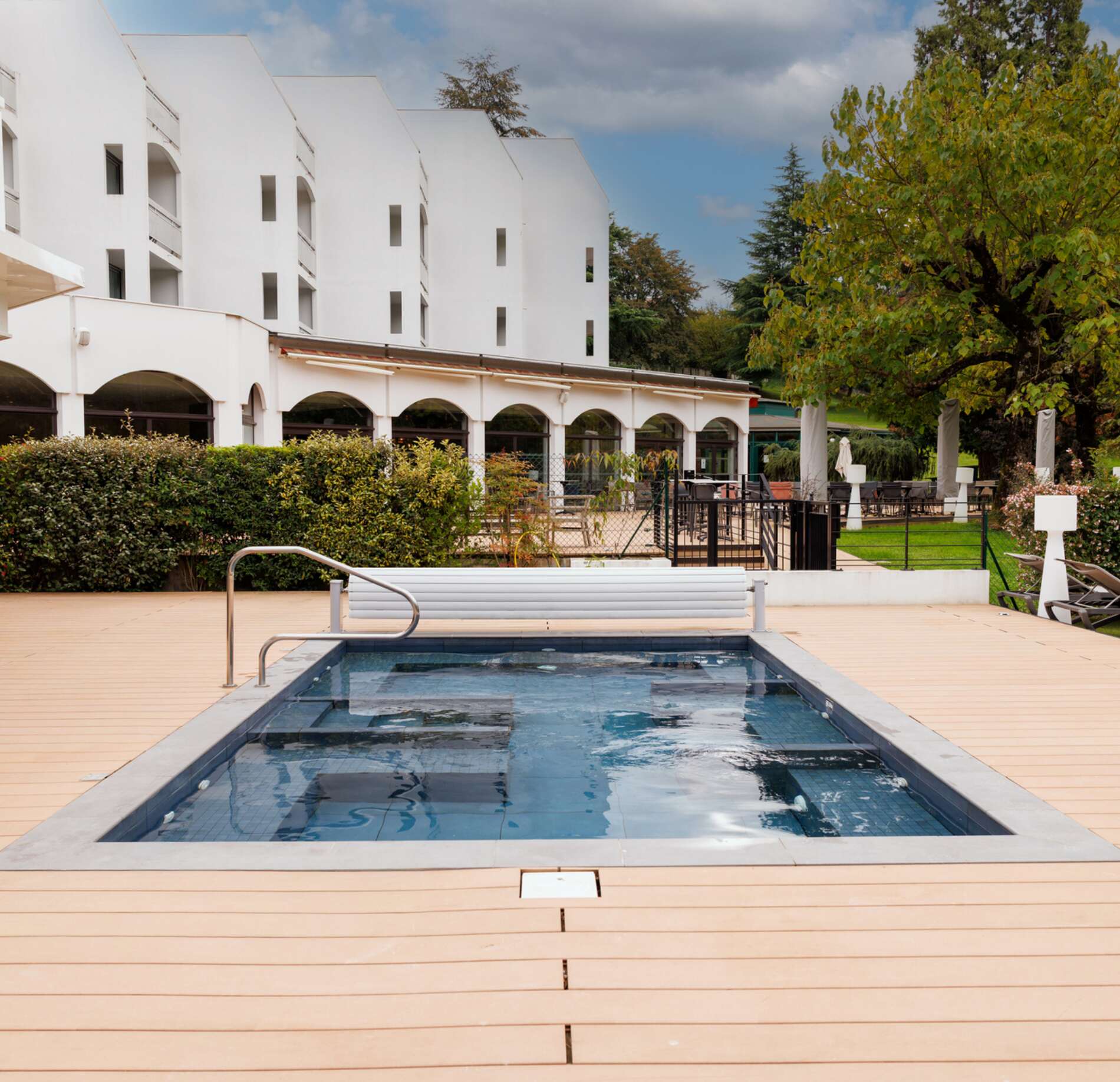 Espace extérieur élégant du domaine Marlioz avec bassin de balnéothérapie moderne, entouré d’une terrasse en bois clair, arbres verdoyants et architecture contemporaine lumineuse, créant une atmosphère calme et raffinée.
