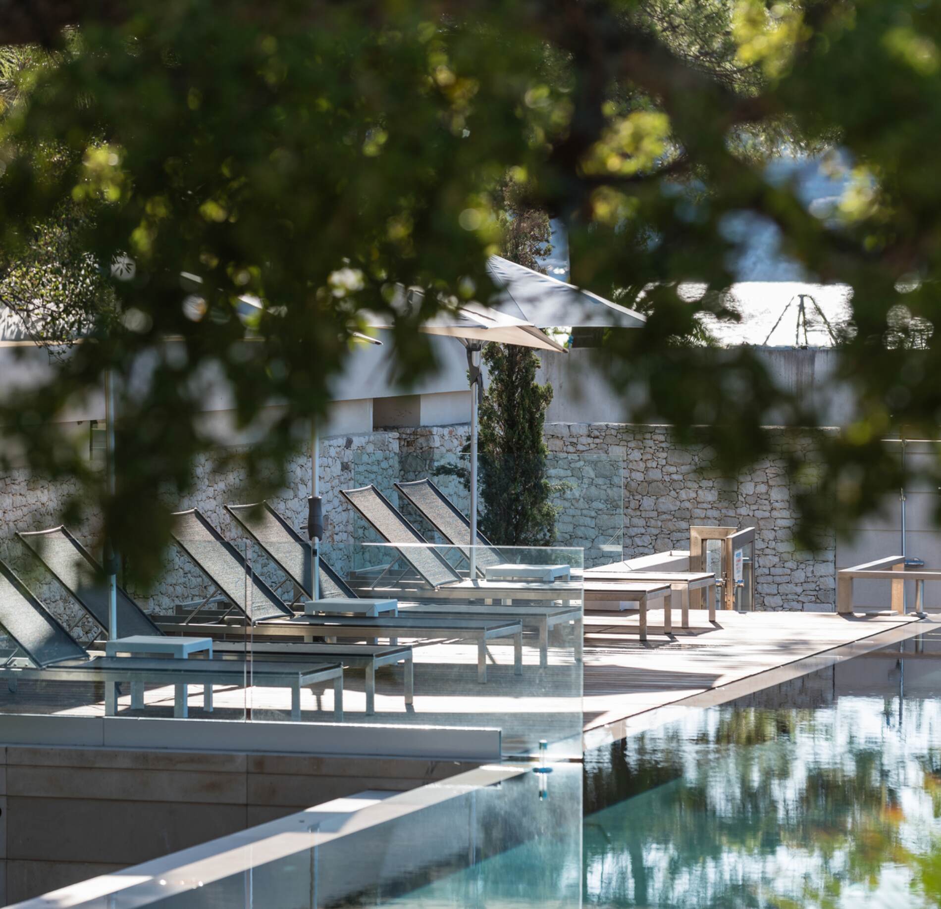 Terrasse élégante du spa NUXE à l’Hôtel Don César, avec transats design disposés autour d’une piscine aux reflets cristallins, entourée de végétation verdoyante et baignée d’une lumière naturelle douce, créant une atmosphère paisible et raffinée. 