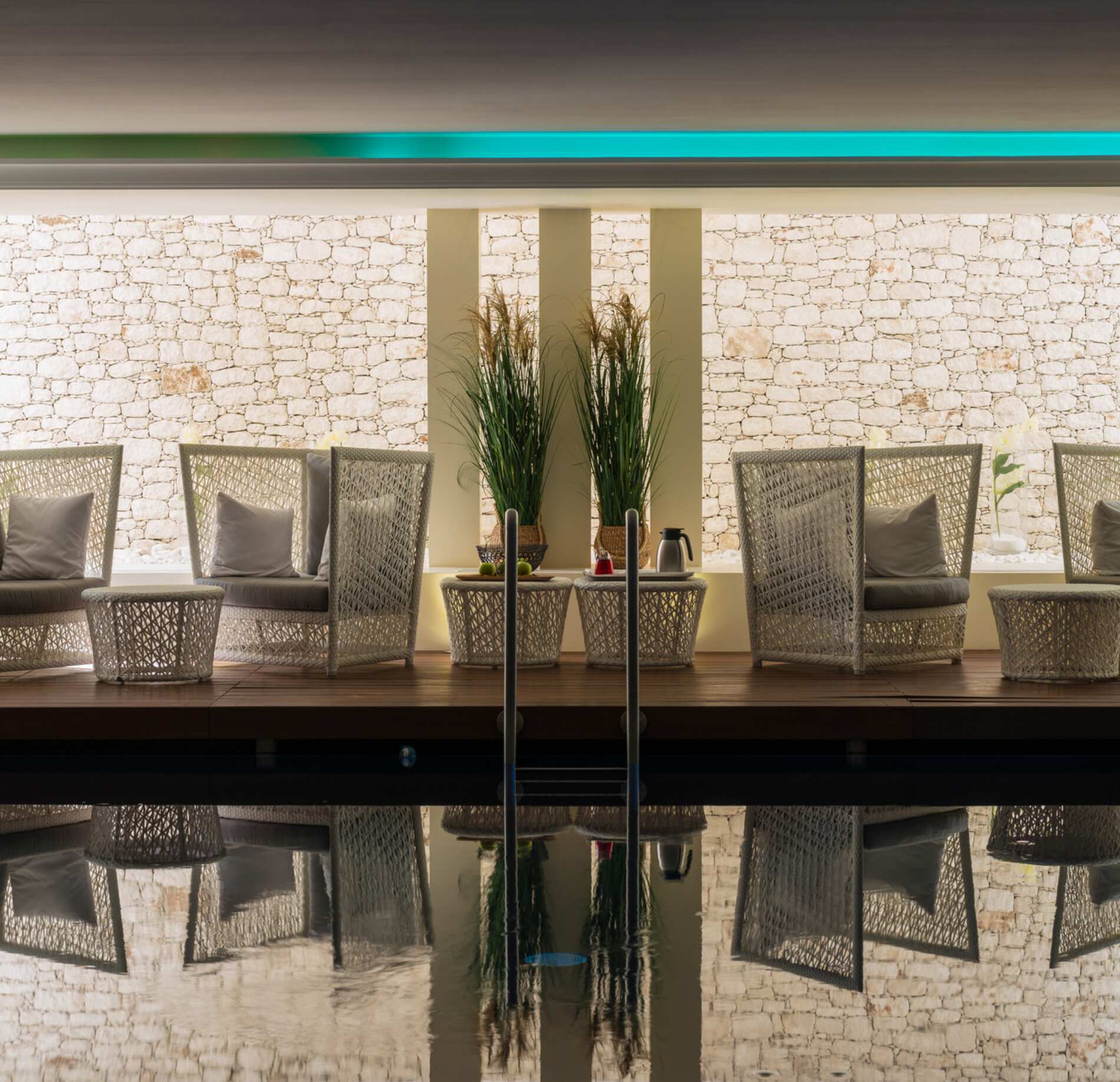 Espace détente élégant du spa NUXE à l’Hôtel Don César, avec fauteuils en fibres naturelles disposés face à une piscine aux reflets apaisants, mur en pierre claire en arrière-plan et éclairage doux créant une atmosphère raffinée et sereine. 