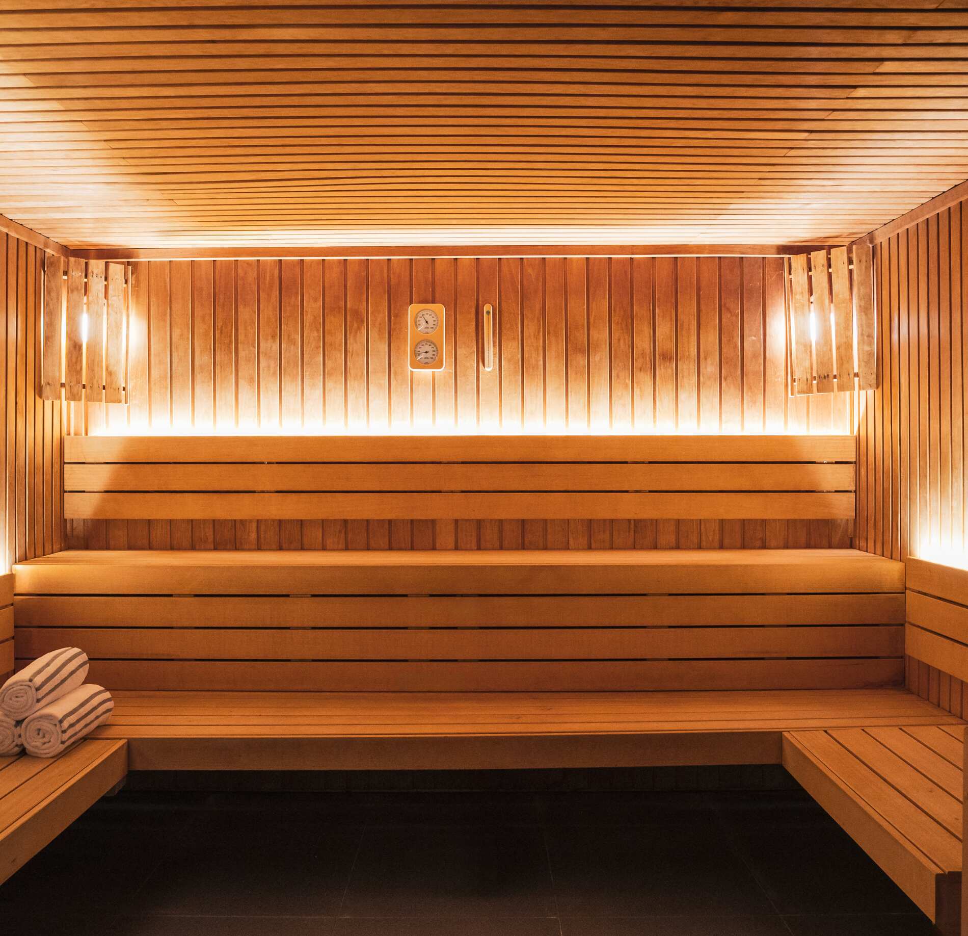 Sauna spacieux et lumineux du spa NUXE à l’Hôtel Héliopic, entièrement habillé de bois chaleureux, avec banquettes en gradins, éclairage doux intégré et serviettes soigneusement disposées, créant une atmosphère enveloppante, élégante et profondément relaxante.