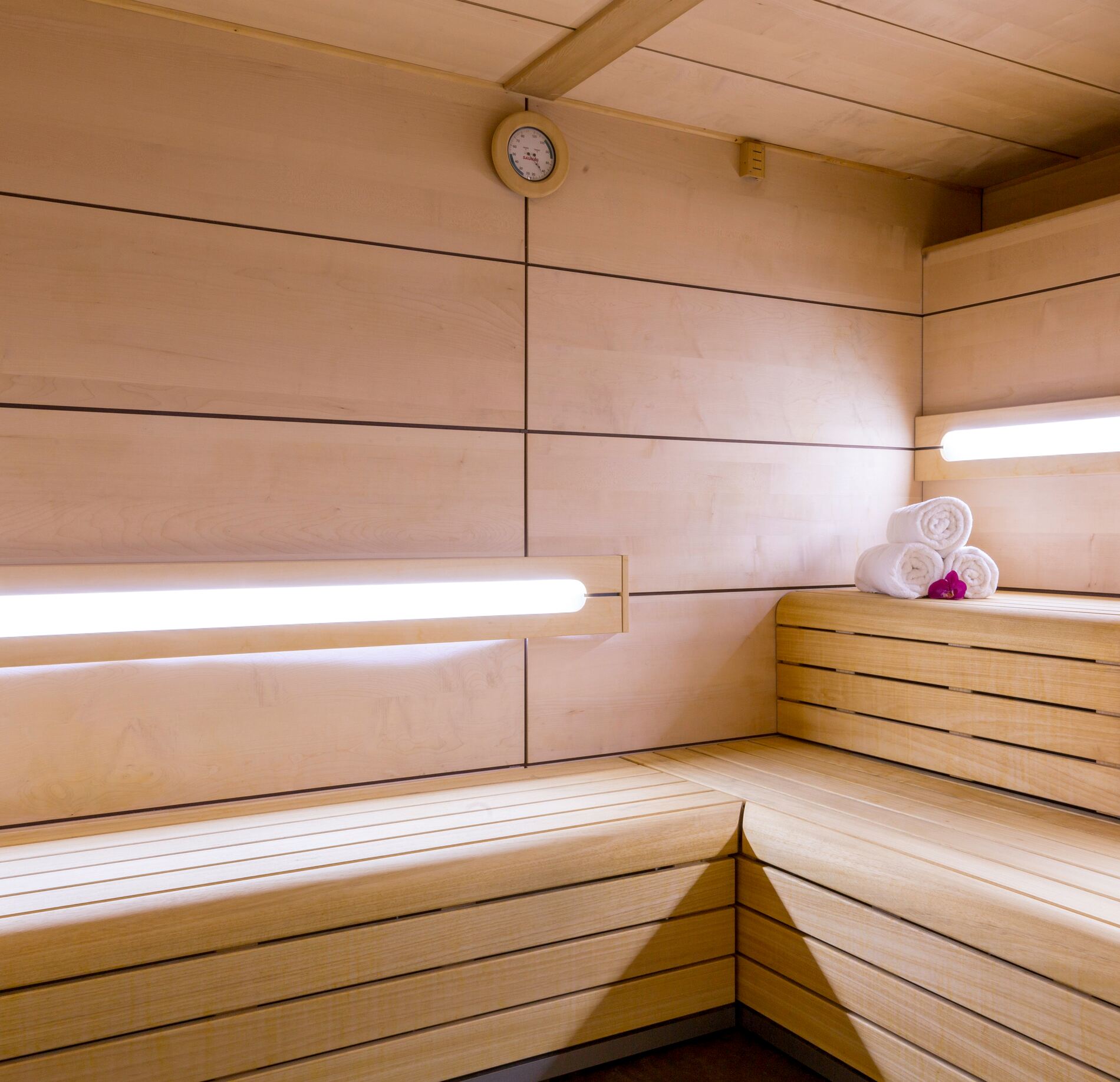 Sauna lumineux du spa NUXE à l’Hôtel de la Poste Troyes, habillé de bois clair avec banquettes en gradins, éclairage linéaire doux et serviettes soigneusement disposées, créant une atmosphère chaleureuse, épurée et profondément relaxante. 