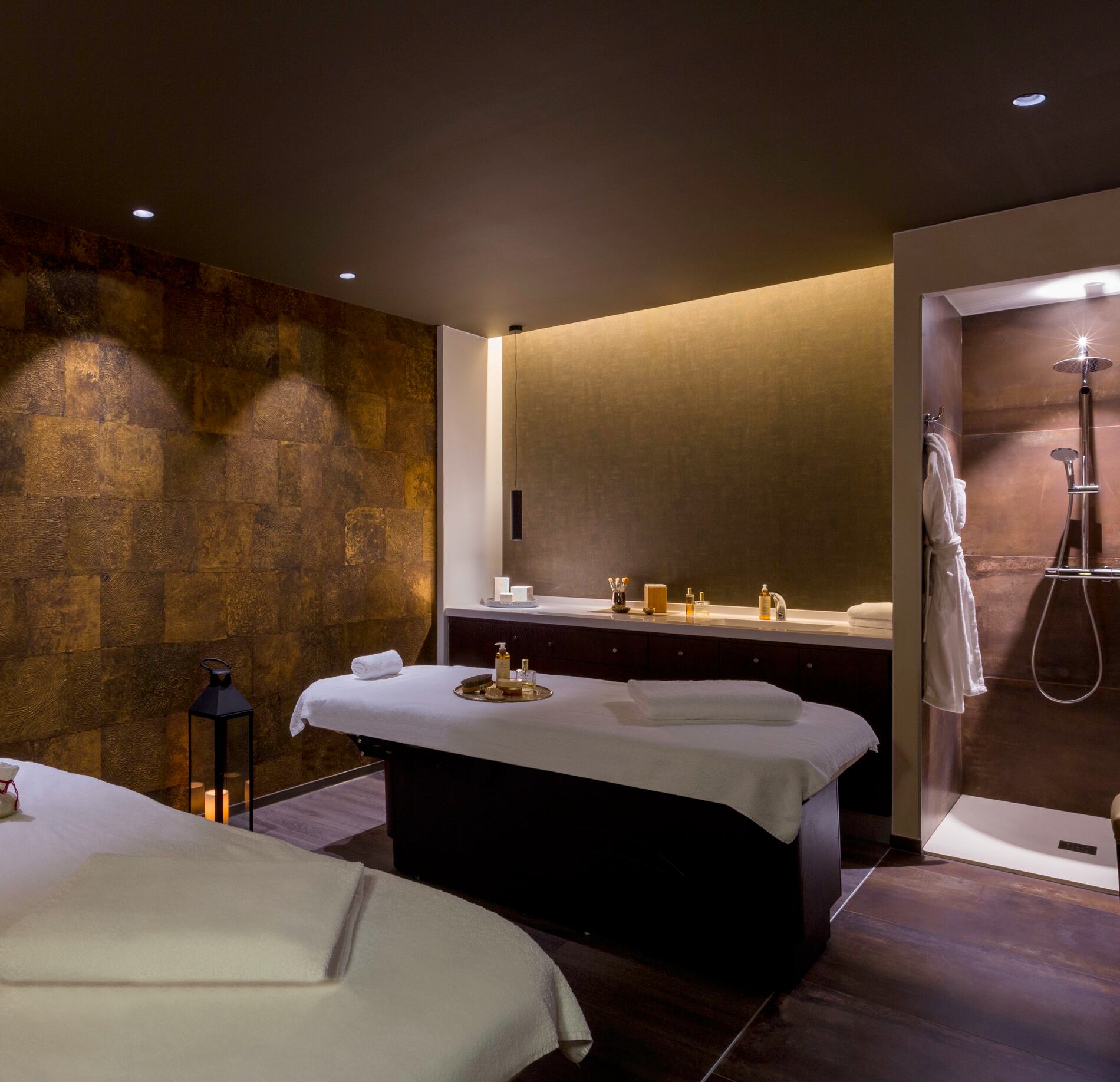 Cabine de soin élégante du spa NUXE à l’Hôtel de la Poste Troyes, avec table de massage confortable, éclairage tamisé, murs aux teintes chaudes et espace douche moderne en arrière-plan, créant une atmosphère intime, raffinée et apaisante. 