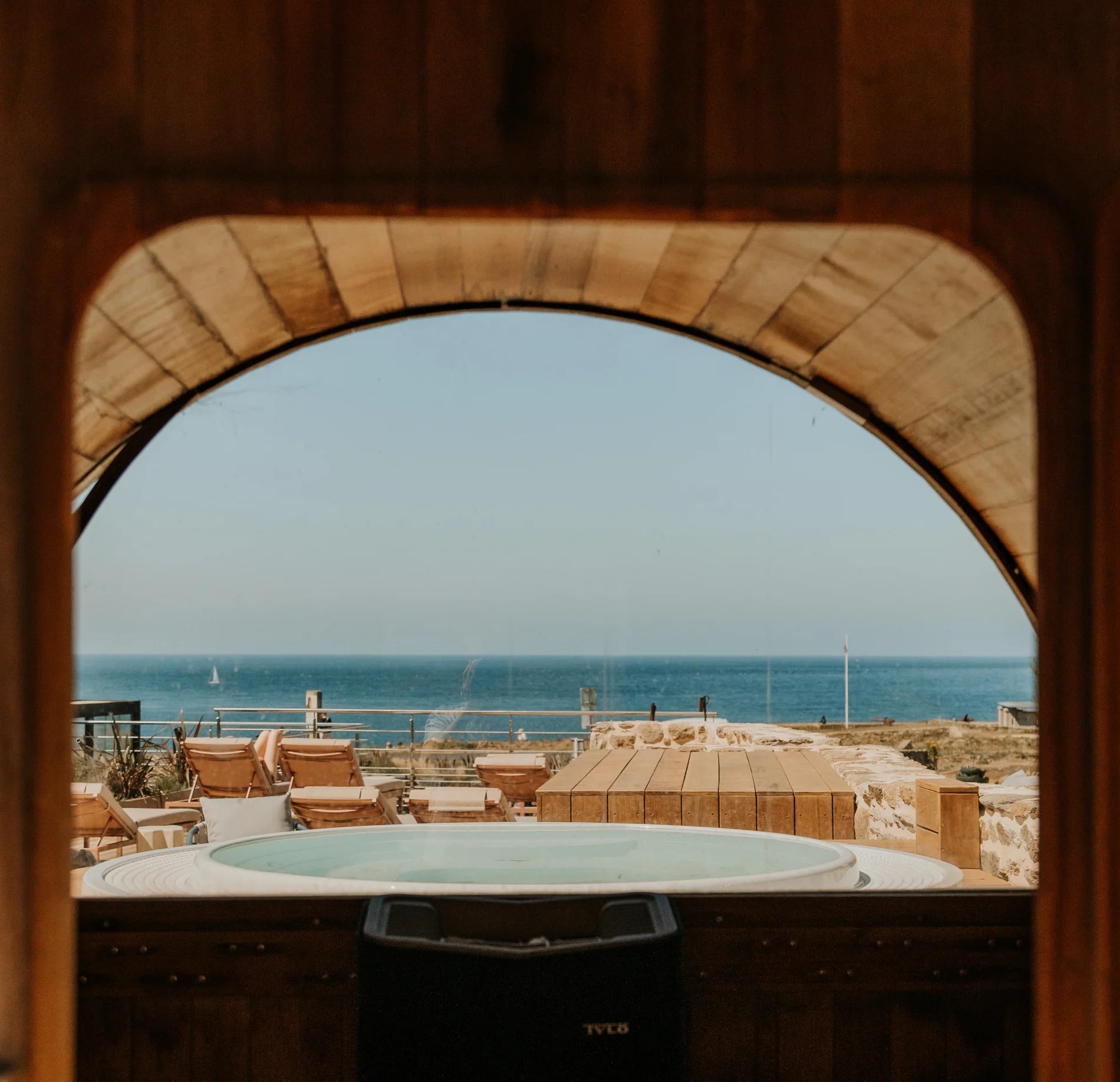 Bain à remous extérieur avec vue sur la mer, entouré de transats et d’une terrasse aménagée.