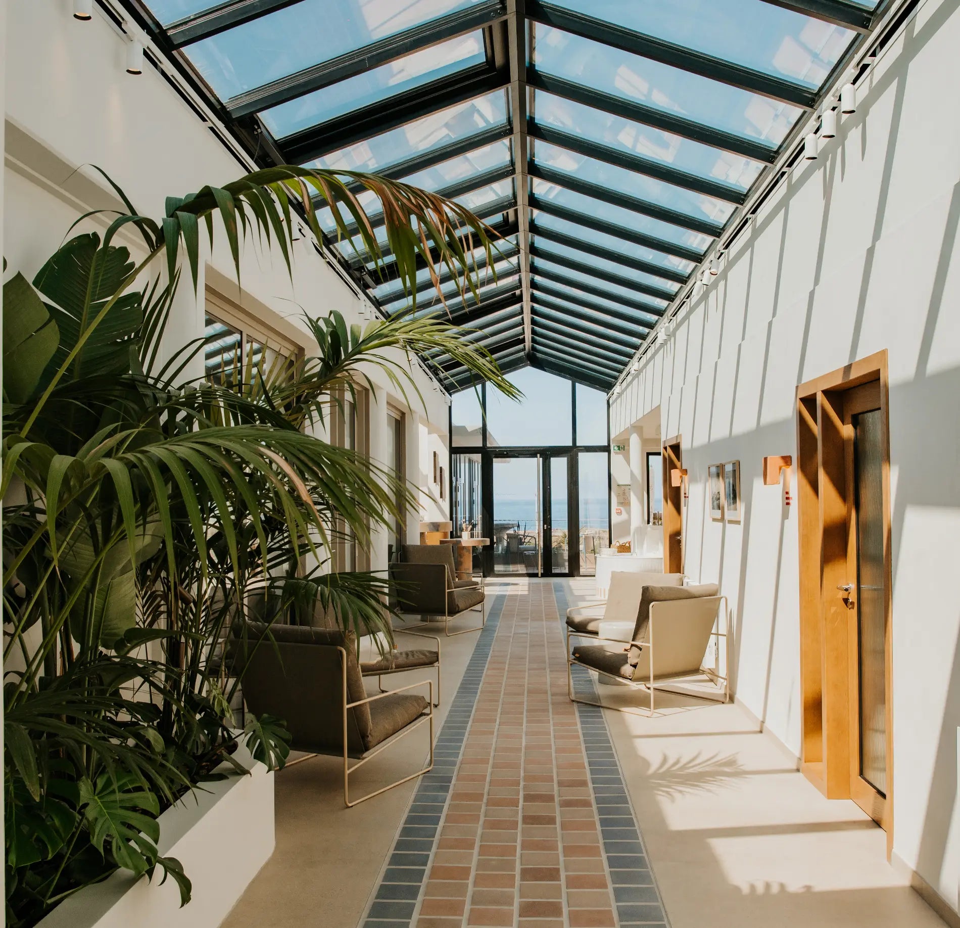 Hall de spa lumineux avec verrière, fauteuils et plantes disposés le long d’un espace de détente intérieur.