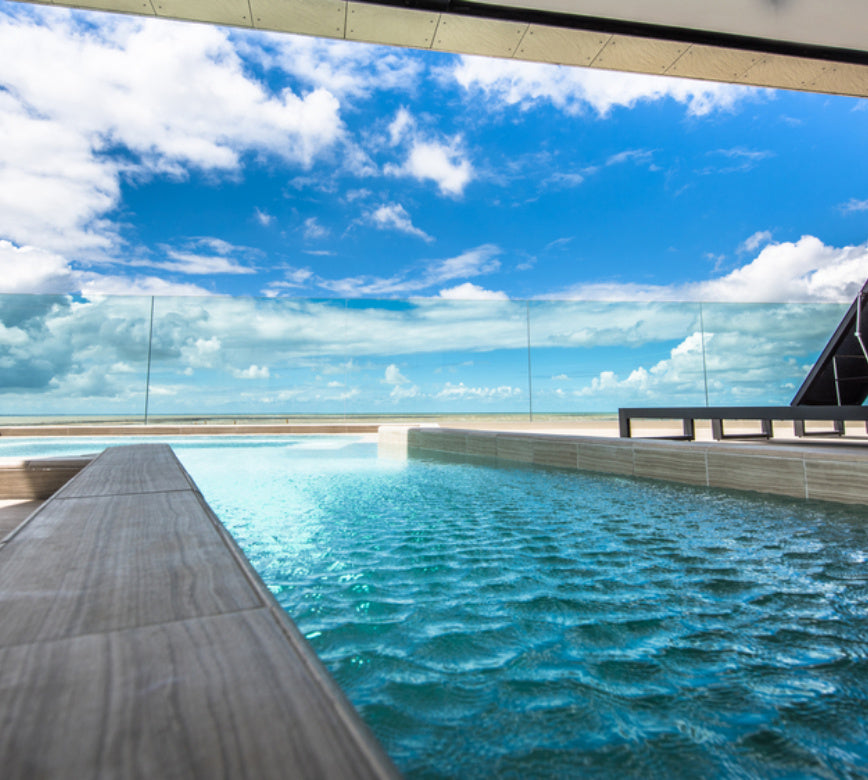 Bassin extérieur du spa NUXE à La Grande Terrasse, bordé d’une terrasse en bois aux lignes épurées, avec eau aux reflets miroitants et garde-corps en verre laissant apparaître un horizon marin infini sous un ciel éclatant, offrant un cadre lumineux, serein et haut de gamme propice à la détente.