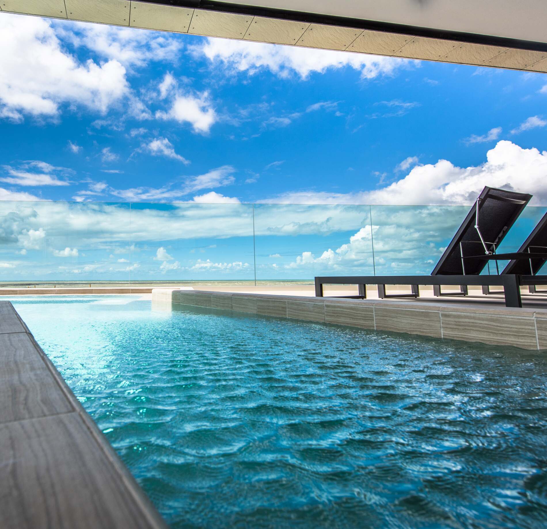 Piscine extérieure panoramique du spa NUXE à La Grande Terrasse, avec eau aux reflets turquoise, terrasse moderne en bois et transat design face à l’océan sous un ciel bleu lumineux, créant une atmosphère élégante, apaisante et ouverte sur l’horizon.