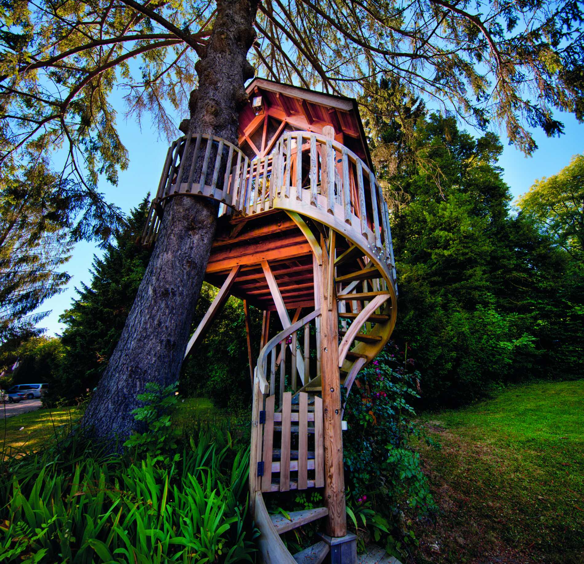 Cabane perchée en bois du spa NUXE à l’Hôtel La Licorne, construite autour d’un grand arbre avec escalier en colimaçon et terrasse circulaire, nichée au cœur d’un jardin verdoyant sous un ciel lumineux, créant une atmosphère naturelle, insolite et ressourçante.
