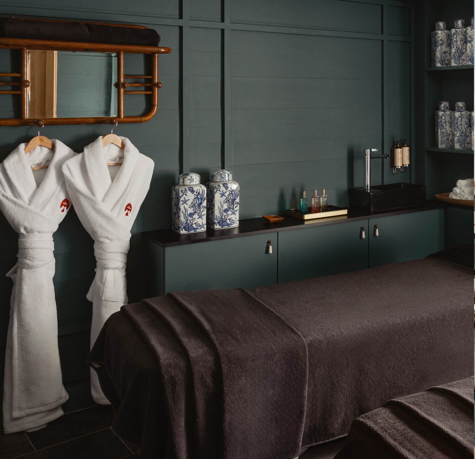 Cabine de soin élégante du spa NUXE à l’Hôtel La Mission, avec tables de massage habillées de linge brun, peignoirs blancs suspendus, céramiques décoratives et éclairage doux, créant une atmosphère intime, raffinée et apaisante.