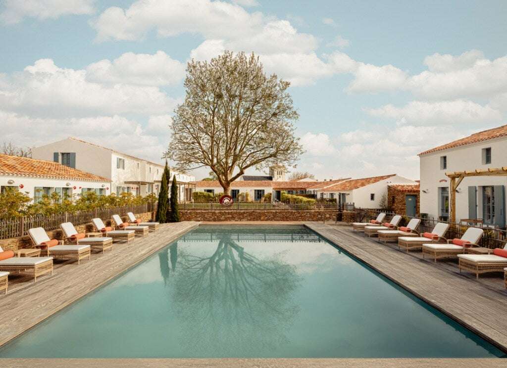 Grande piscine extérieure entourée de transats confortables, au cœur d’un domaine de charme aux façades blanches, offrant un cadre paisible propice à la détente et au bien-être.