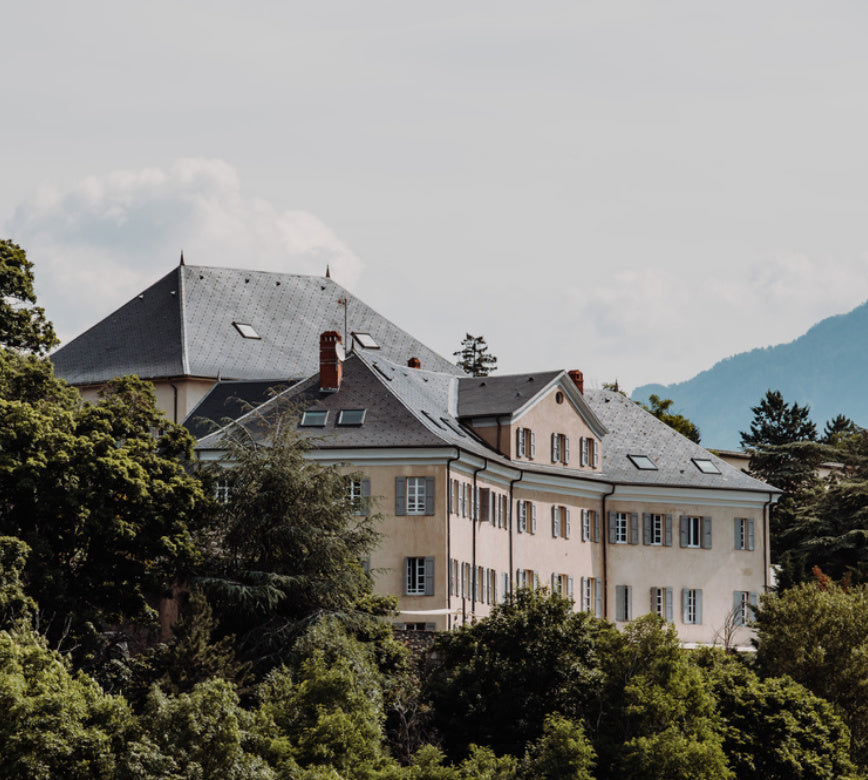 Domaine de caractère abritant le spa NUXE à l’Hôtel La Robeyère, composé d’un bâtiment aux lignes classiques, toitures en ardoise et fenêtres harmonieuses, entouré d’arbres verdoyants et ouvert sur un paysage de montagnes, sous une lumière douce offrant un cadre serein, élégant et haut de gamme.