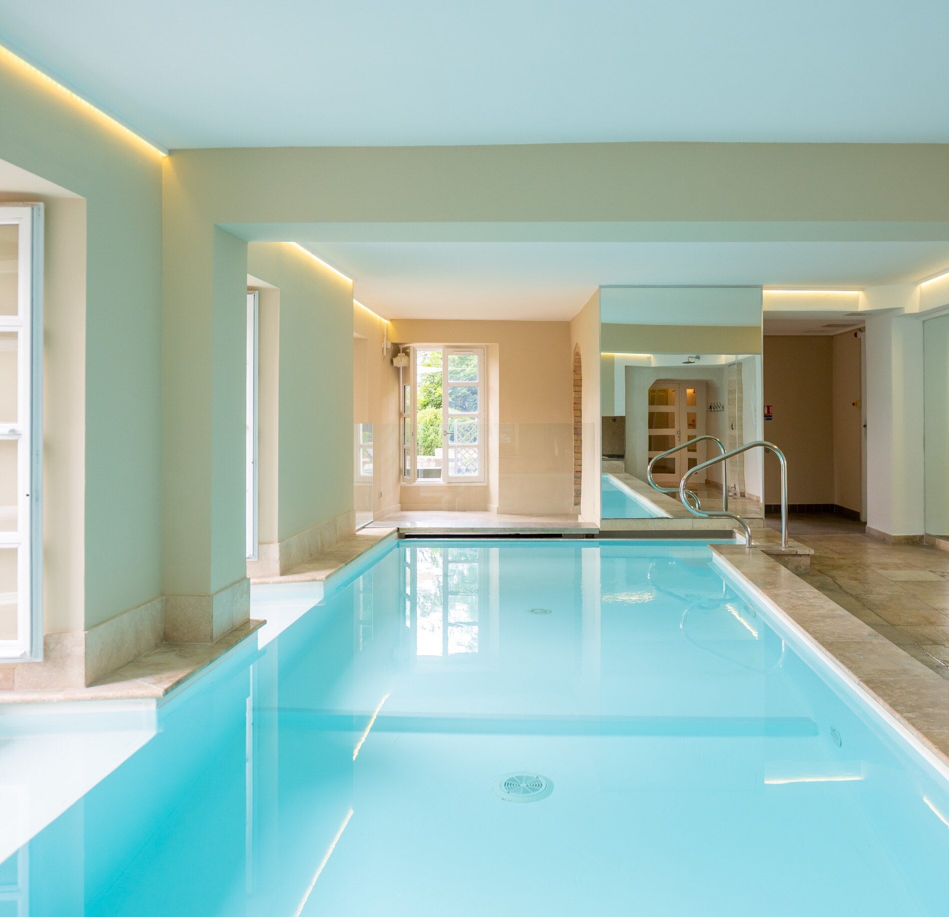Piscine intérieure lumineuse du spa NUXE à l’Hôtel La Robeyère, avec bassin aux reflets turquoise, architecture épurée aux tons clairs, éclairage indirect élégant et ouvertures laissant entrer la lumière naturelle, créant une atmosphère calme, raffinée et apaisante. 