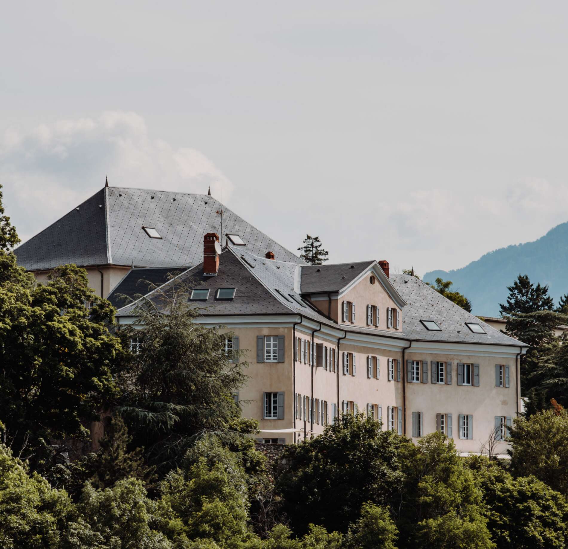 Élégante bâtisse du spa NUXE à l’Hôtel La Robeyère, aux façades claires et volets traditionnels, nichée au cœur d’un écrin de verdure avec vue sur les montagnes en arrière-plan, sous une lumière douce créant une atmosphère paisible et raffinée.